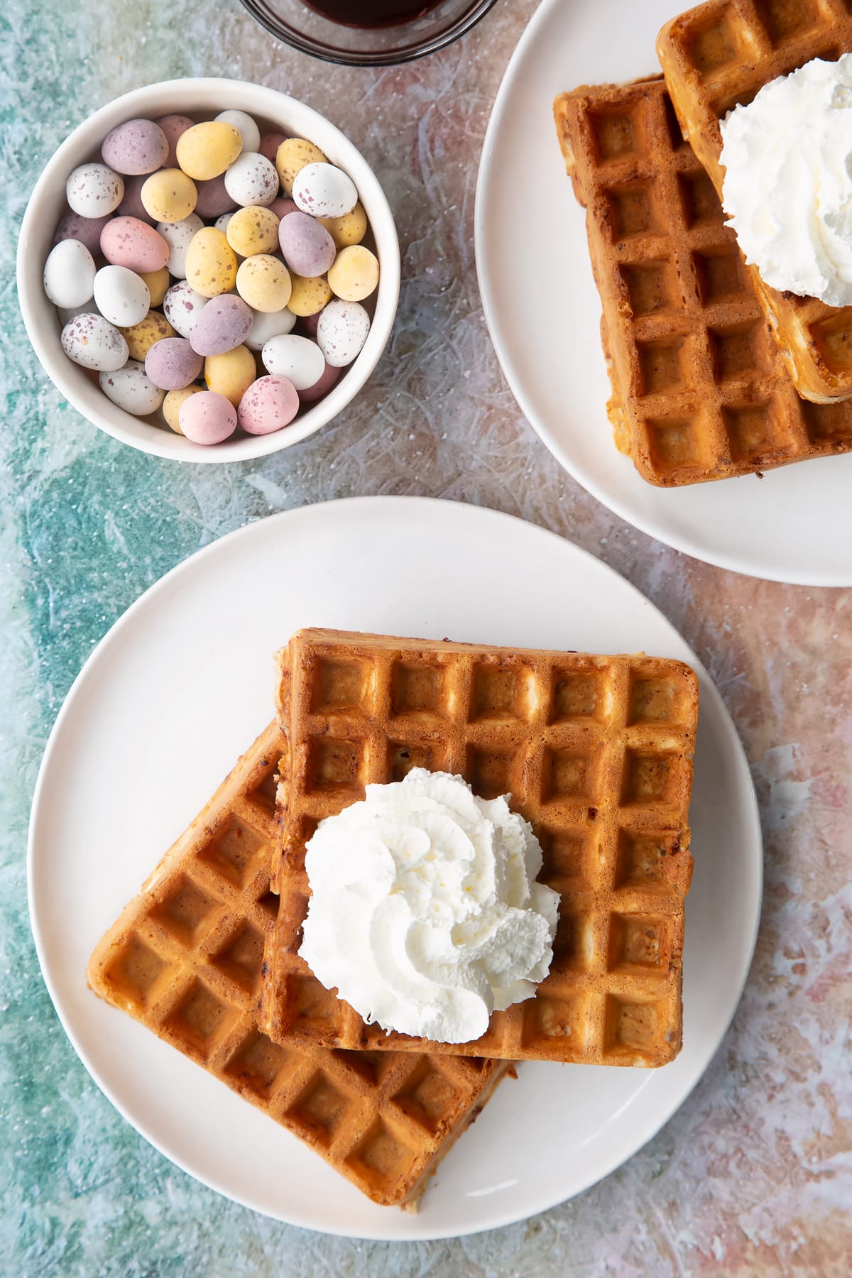 Mini egg waffles on a white plate. They are topped with squirty cream.