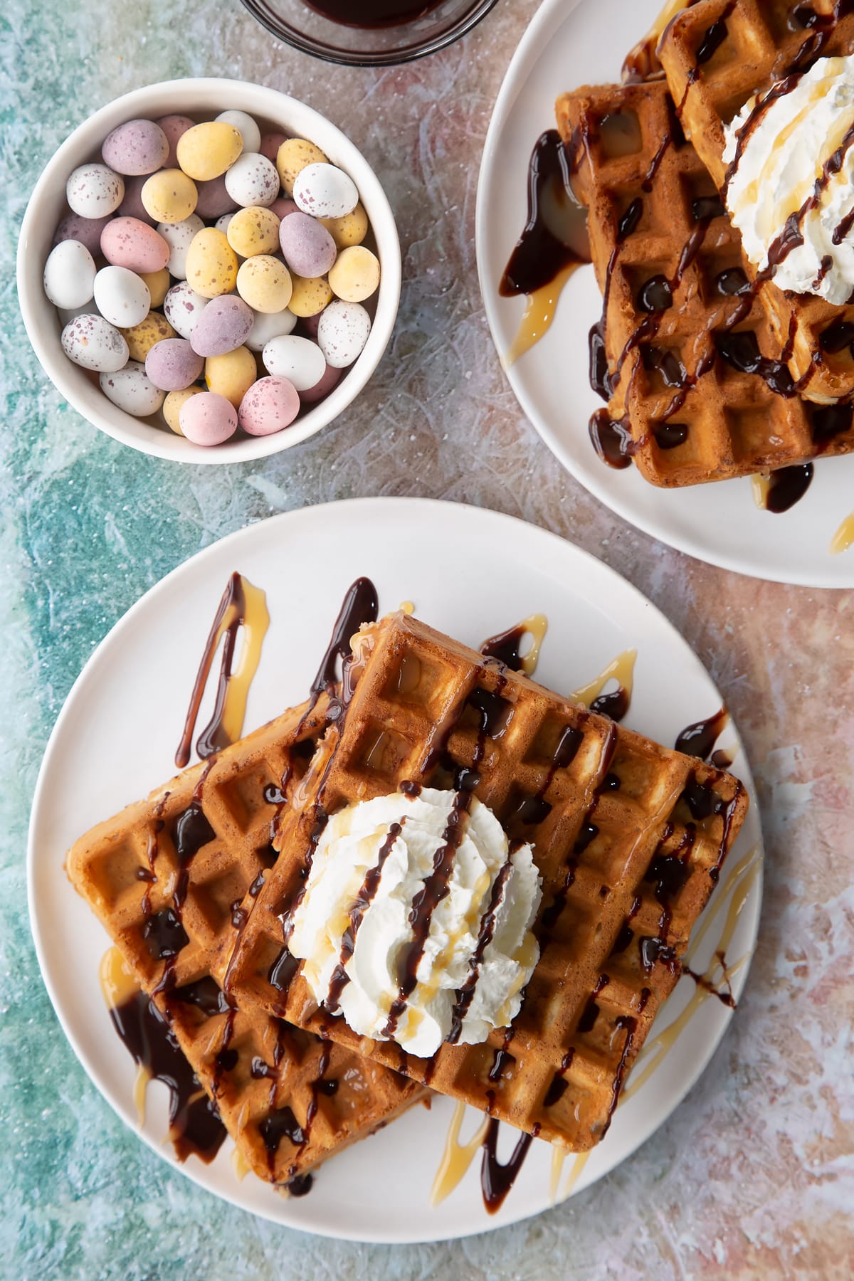 Mini egg waffles on a white plate. They are topped with squirty cream, chocolate sauce and toffee sauce.