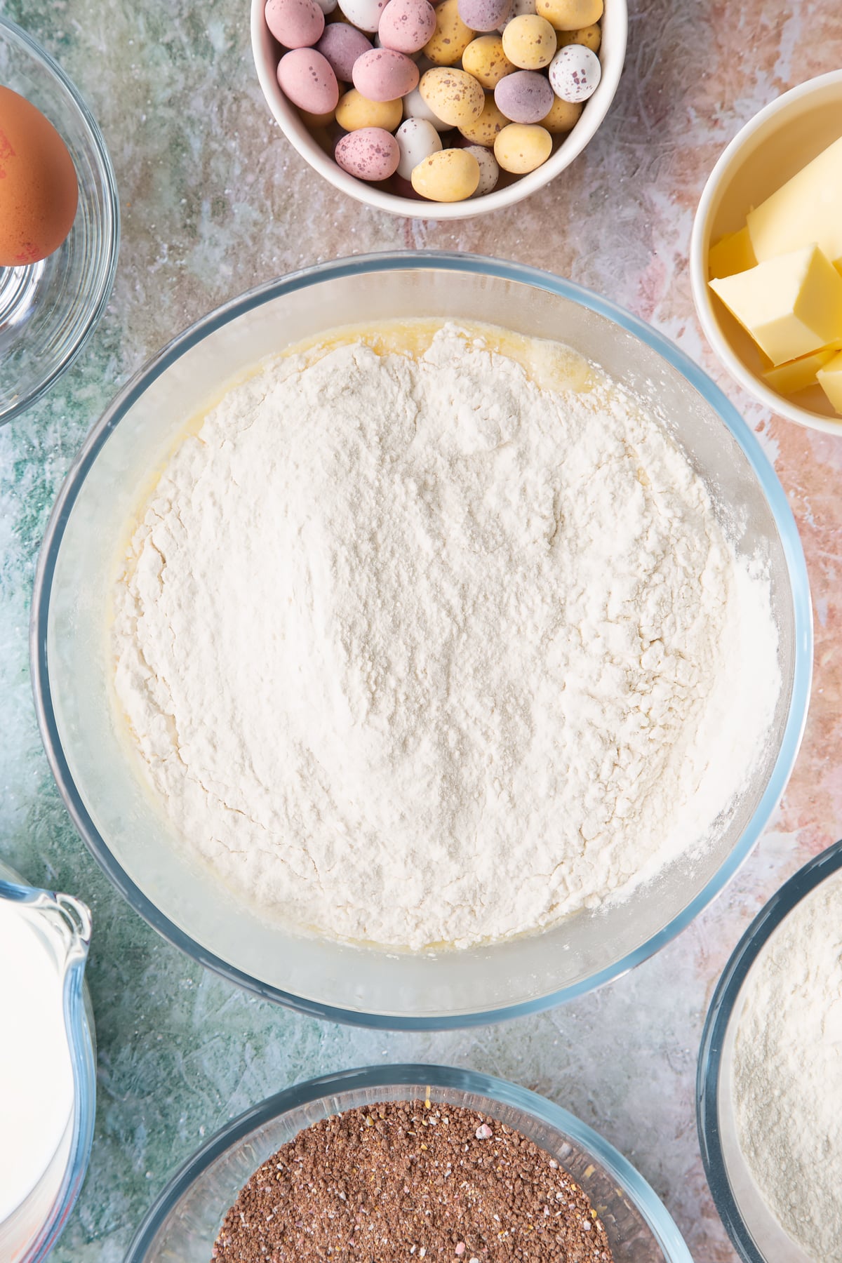 Melted butter, milk and eggs whisked together in a bowl with self-raising flour on top. Ingredients to make Mini egg waffles surround the bowl.