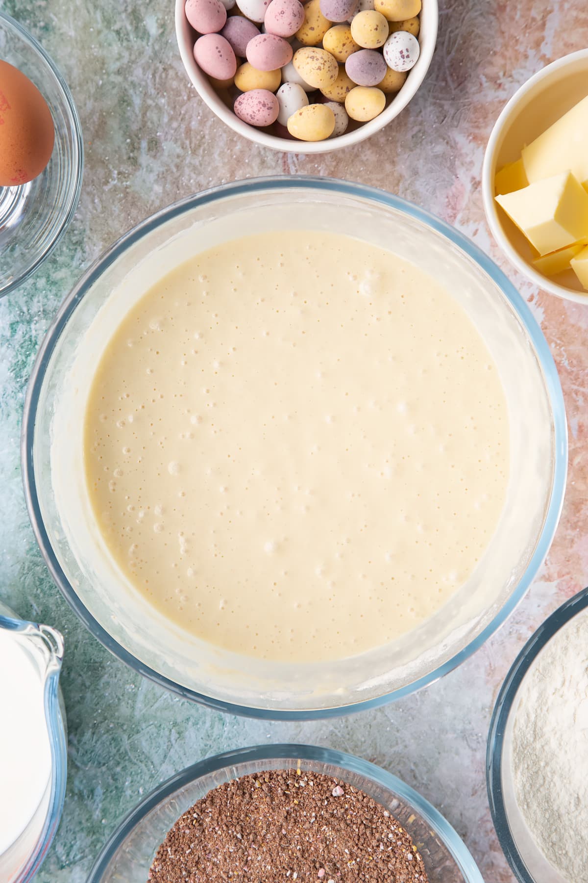 Waffle batter in a bowl. Ingredients to make Mini egg waffles surround the bowl.