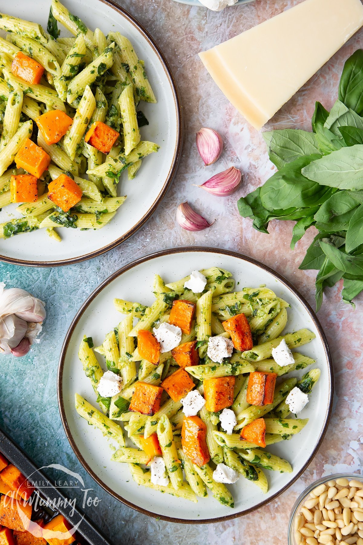 Penne with butternut squash and goat cheese on two grey plates, shown from above.