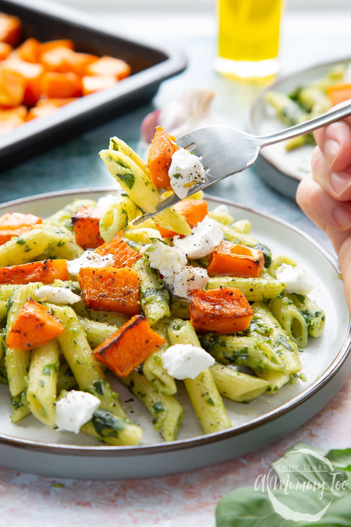 Penne with butternut squash and goat cheese on a grey plate. A hand takes some with a fork.