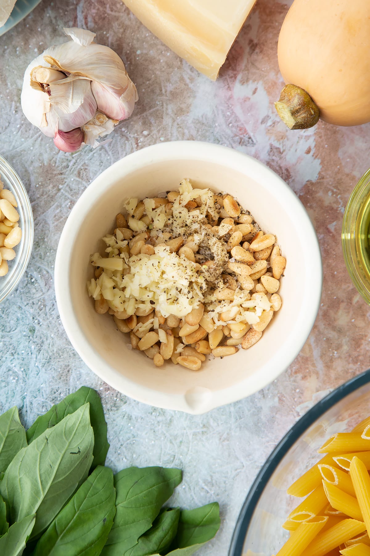 Toasted pine nuts, garlic and pepper in a small mortar. Ingredients to make penne with butternut squash and goat cheese surround the mortar.