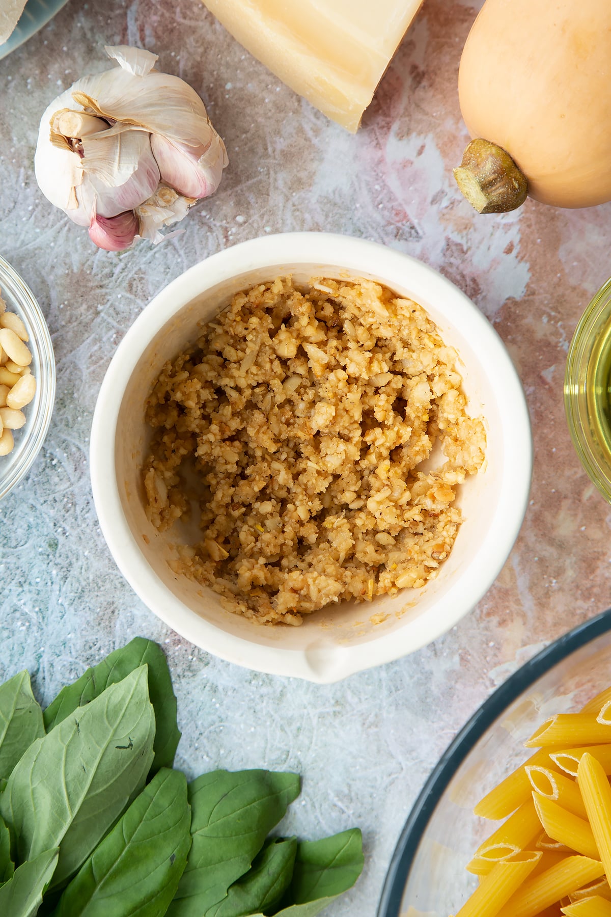 Toasted pine nuts, garlic and pepper crushed in a small mortar. Ingredients to make penne with butternut squash and goat cheese surround the mortar.