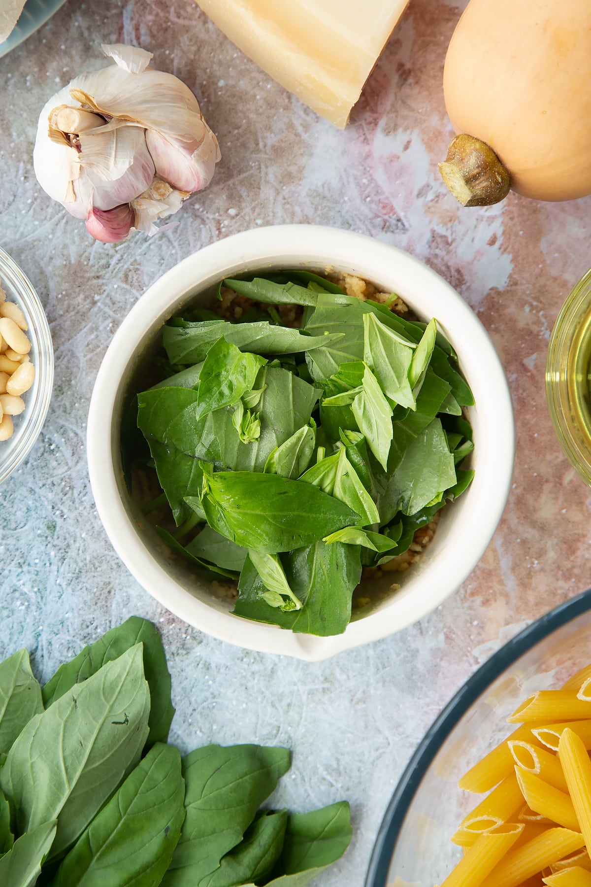 Toasted pine nuts, garlic and pepper crushed in a small mortar with basil leaves on top. Ingredients to make penne with butternut squash and goat cheese surround the mortar.
