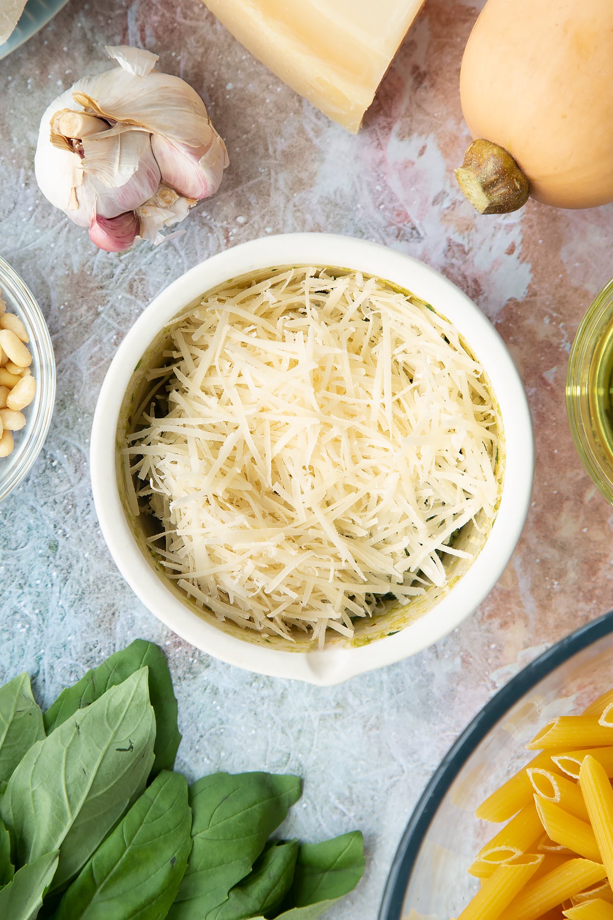 Toasted pine nuts, garlic, pepper and basil crushed in a small mortar with oil and Parmesan on top. Ingredients to make penne with butternut squash and goat cheese surround the mortar.