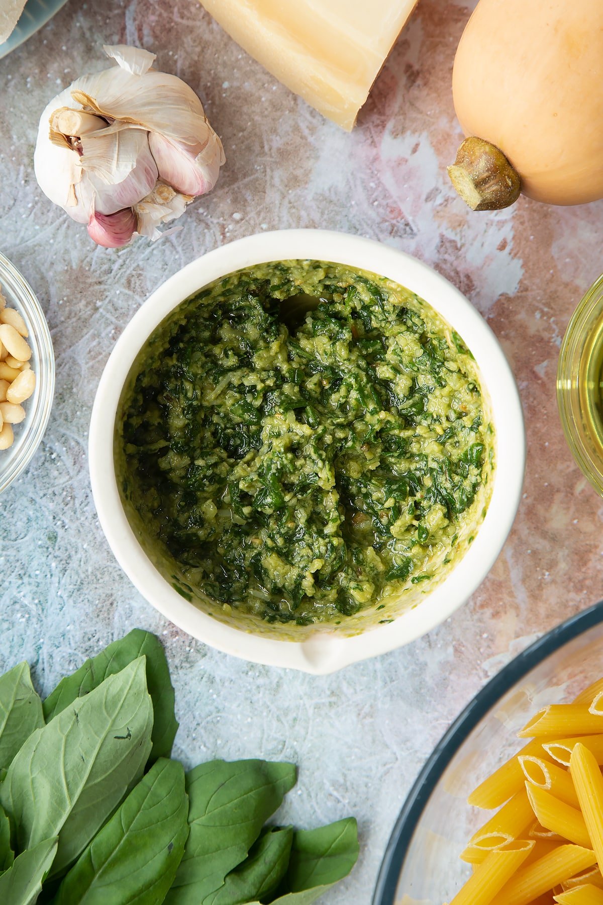 Freshly made pesto in a small mortar. Ingredients to make penne with butternut squash and goat cheese surround the mortar.
