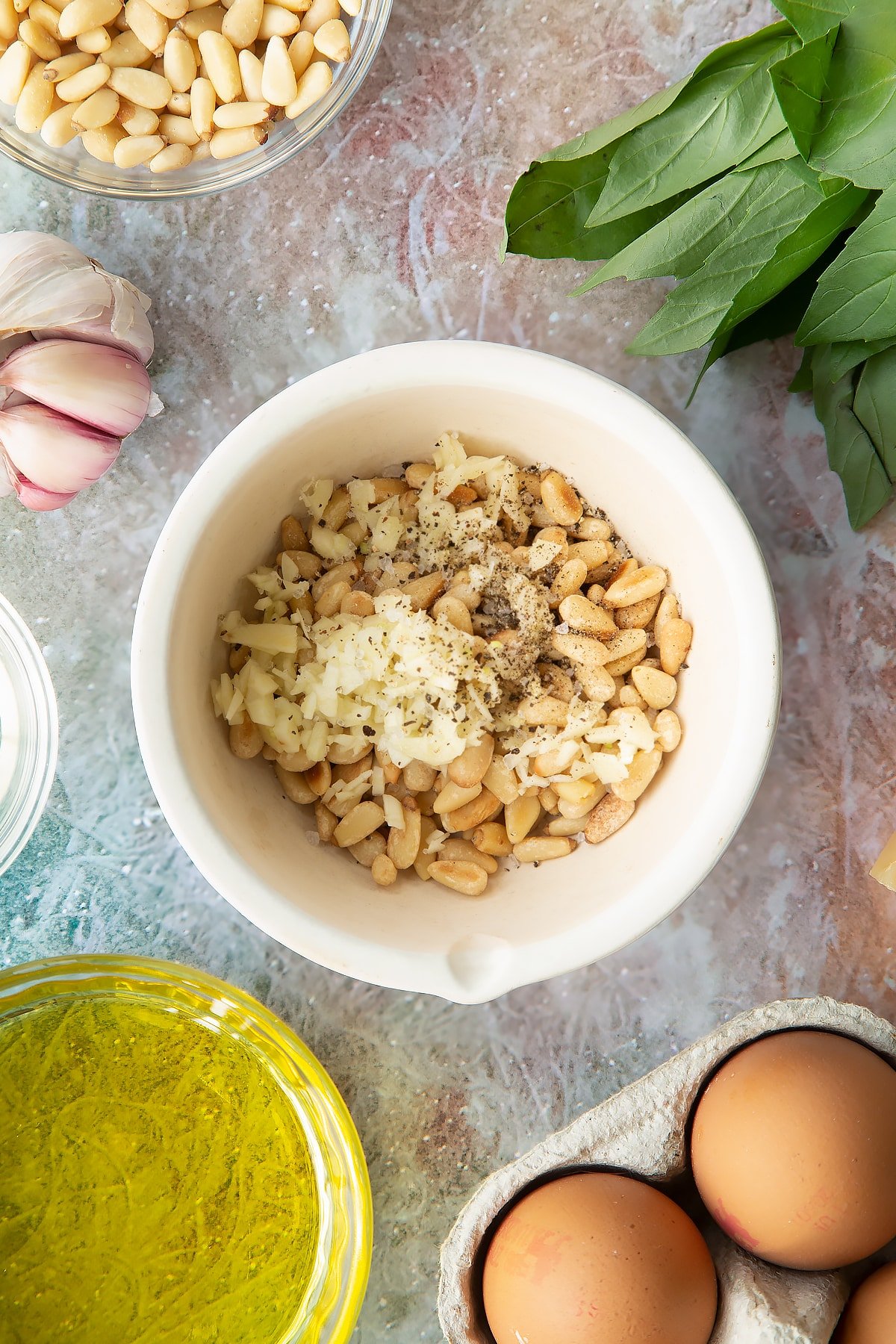 Toasted pine nuts, garlic, salt and pepper in a small mortar. Ingredients to make pesto mayo surround the mortar.