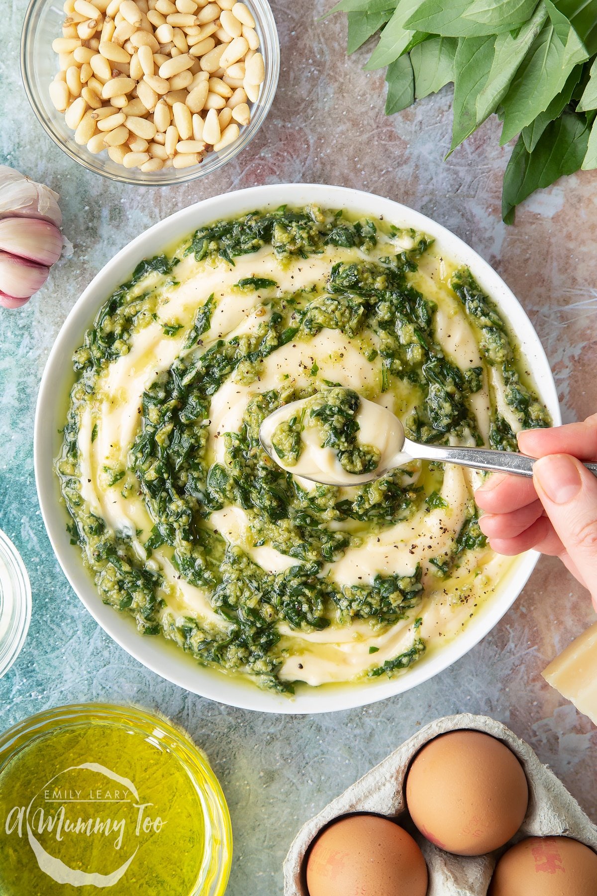Pesto mayo in a white bowl. The pesto and mayonnaise are swirled together. A hand holds a spoonful above the bowl.