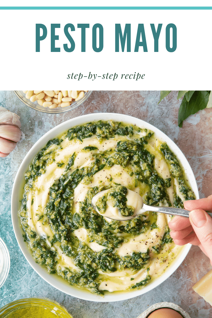 Pesto mayo in a white bowl. A hand holds a spoonful. The pesto and mayonnaise are swirled together. Caption: pesto mayo step-by-step recipe