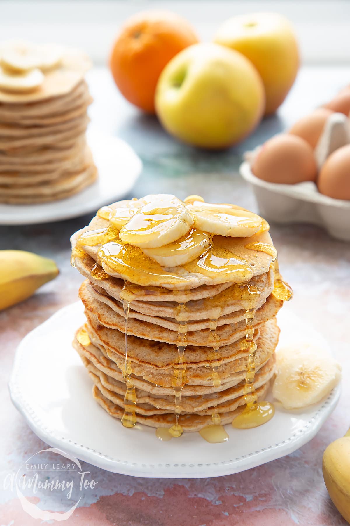 Overhead shot of a pancake stack on a white plate topped with banana and syrup with the A Mummy Too logo in the corner