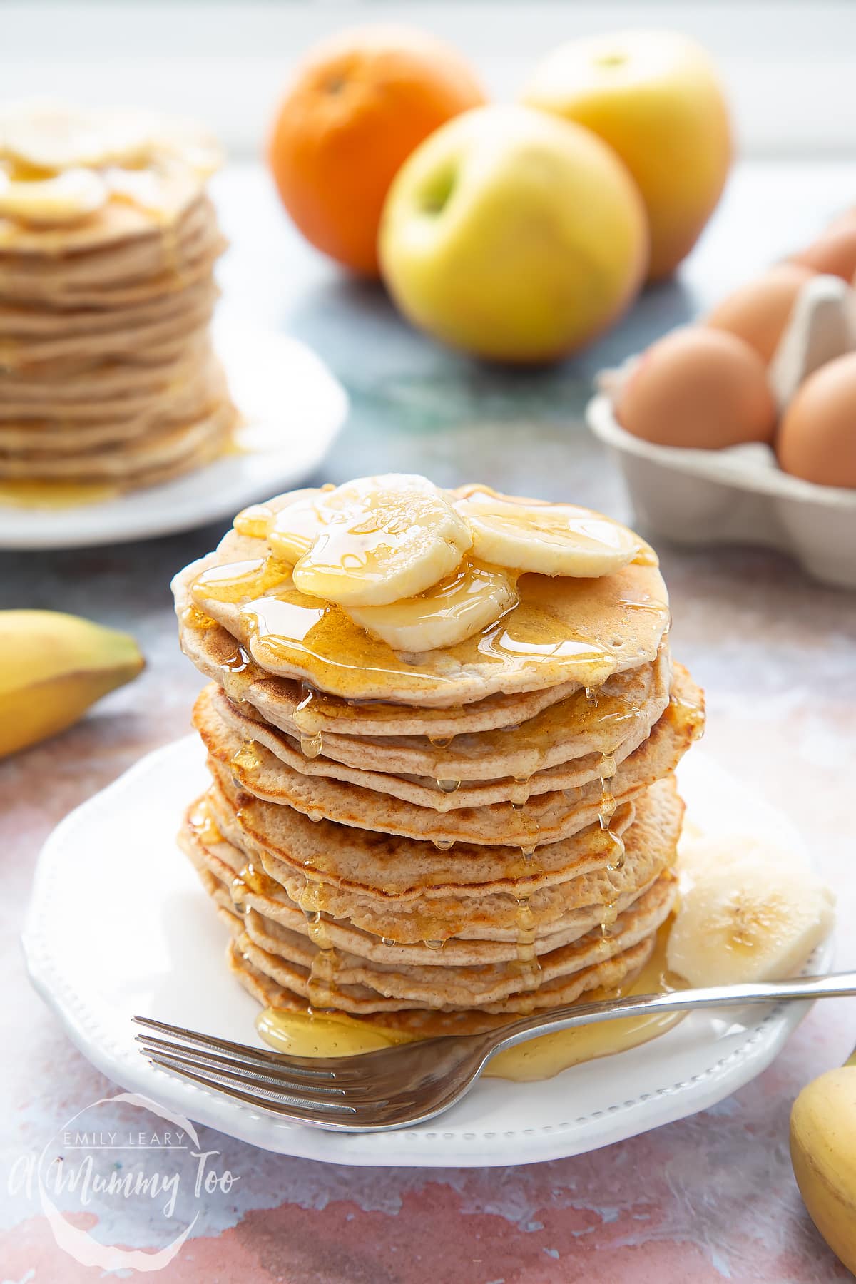 A stack of fluffy pancakes topped with syrup and banana on a white plate and fork