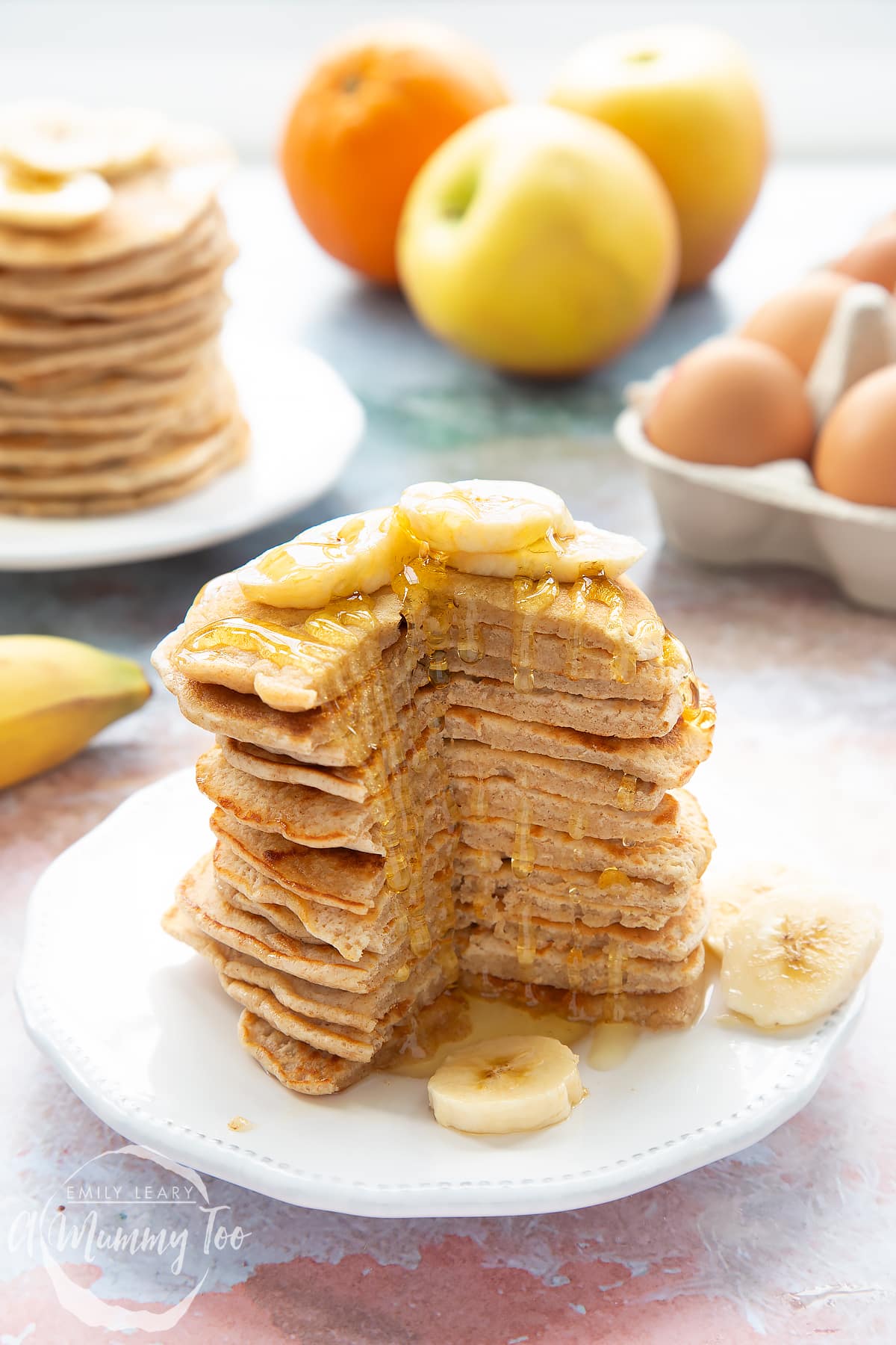 A stack of fluffy pancakes with a cut out of the front topped with syrup and banana on a white plate