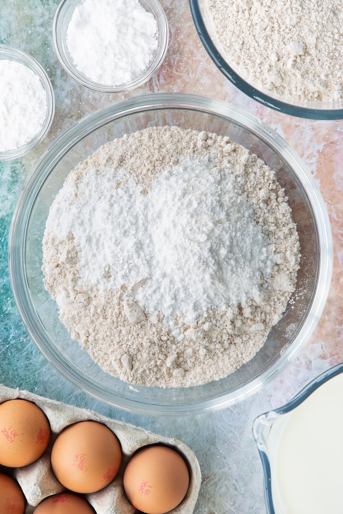 Overhead shot of flour, baking powder, icing sugar and salt in a large clear bowl
