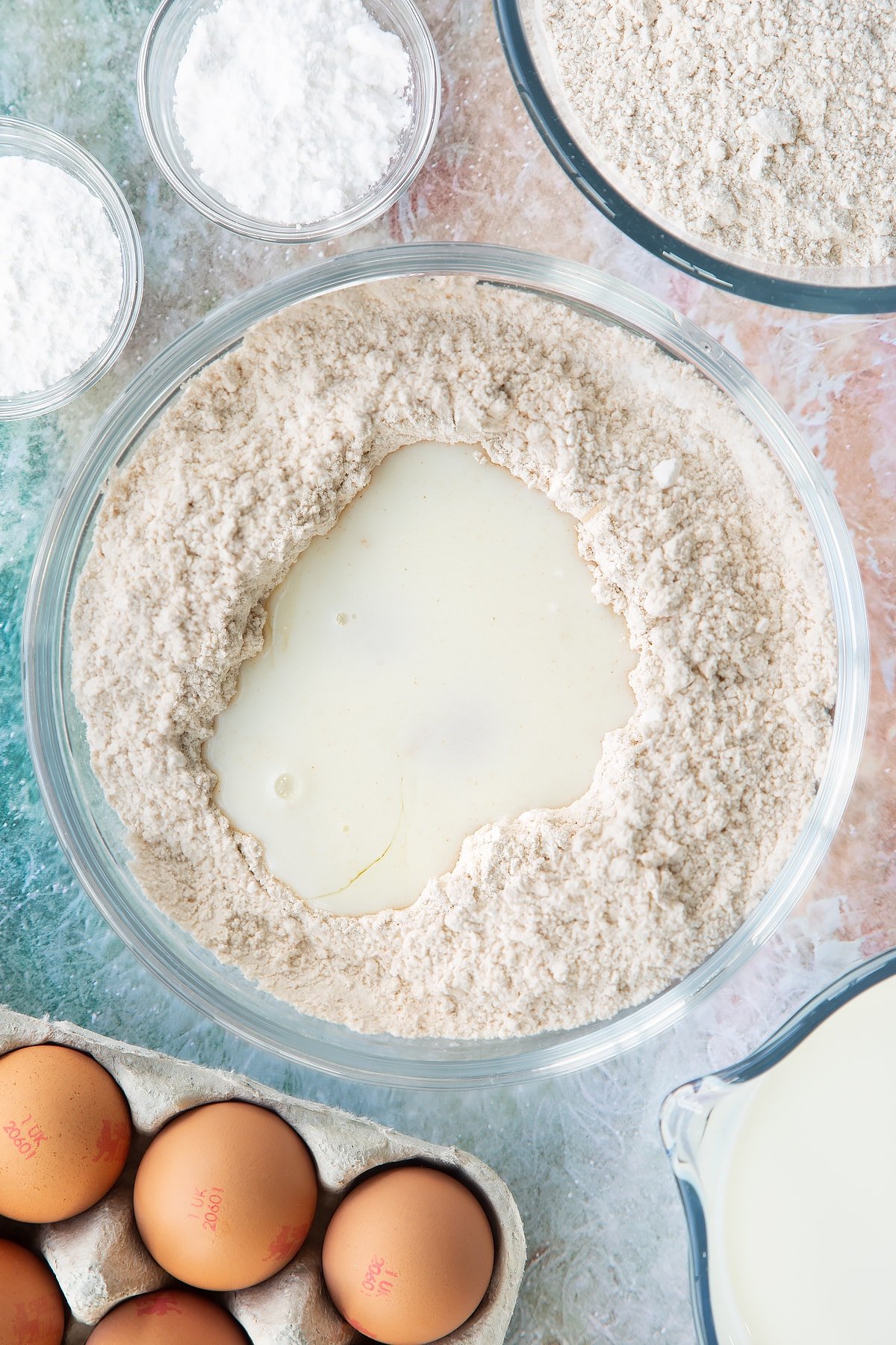 Overhead shot of flour mix with milk and egg in the center of a large clear bowl