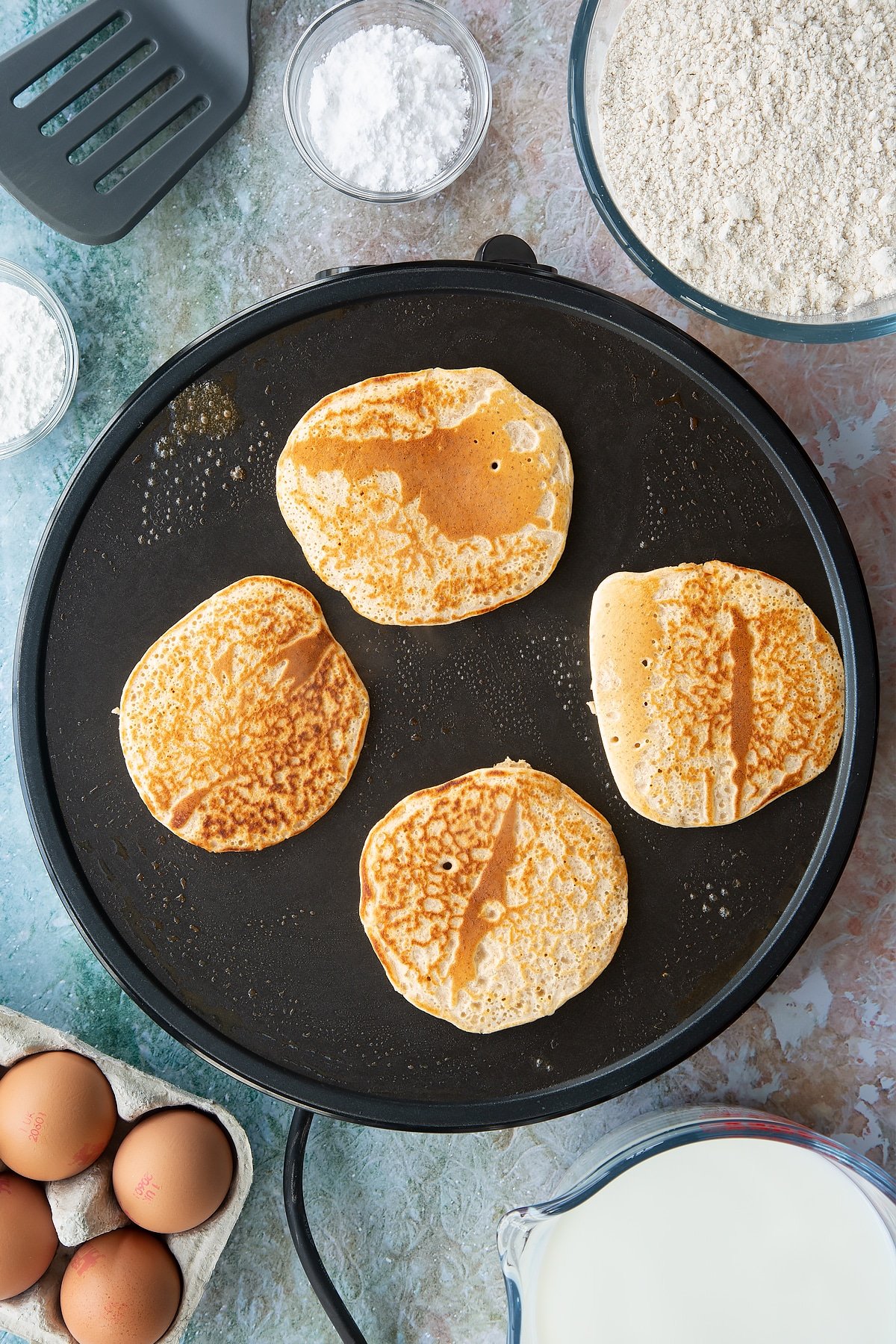 Overhead shot of a hot plate cooking four pancakes cooking