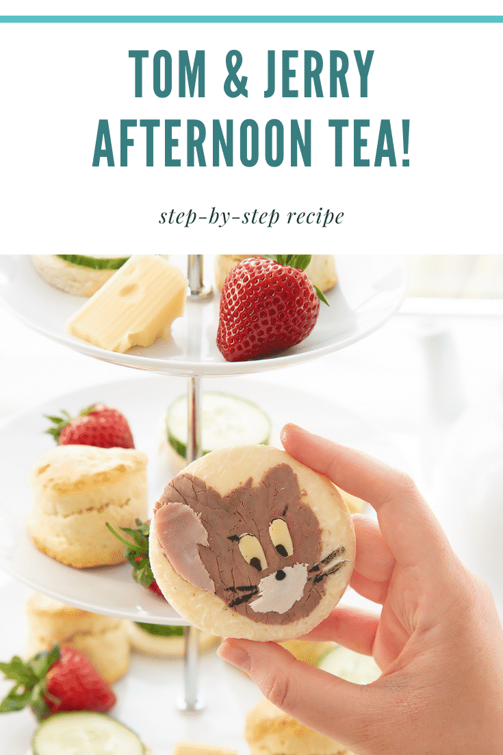 Hand holding a Tom and Jerry sandwhich with a three tier cake stand in the background.