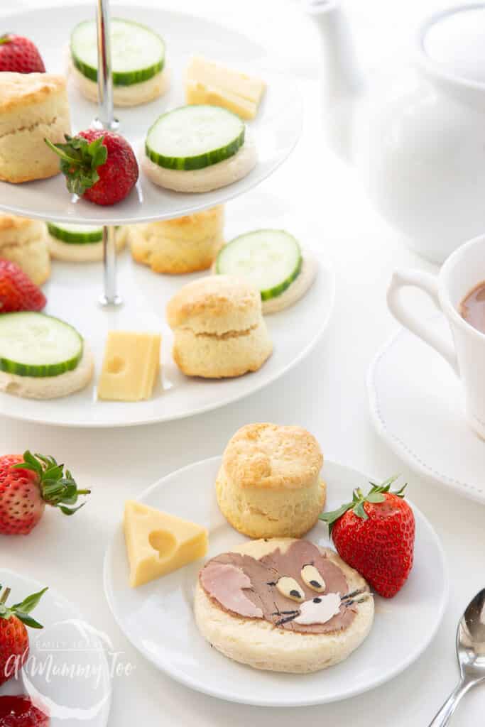 Side on shot of the finished Tom and Jerry afternoon tea with a cake stand, plate of food and a cup of tea on the side.
