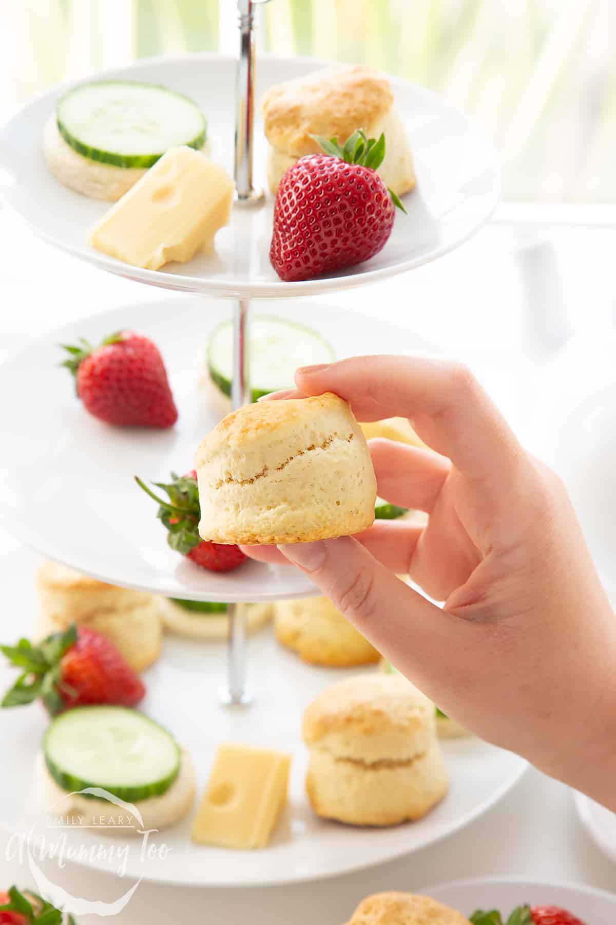 Hand holding a scone with the three tier cake stan from the Tom and Jerry afternoon tea in the background.