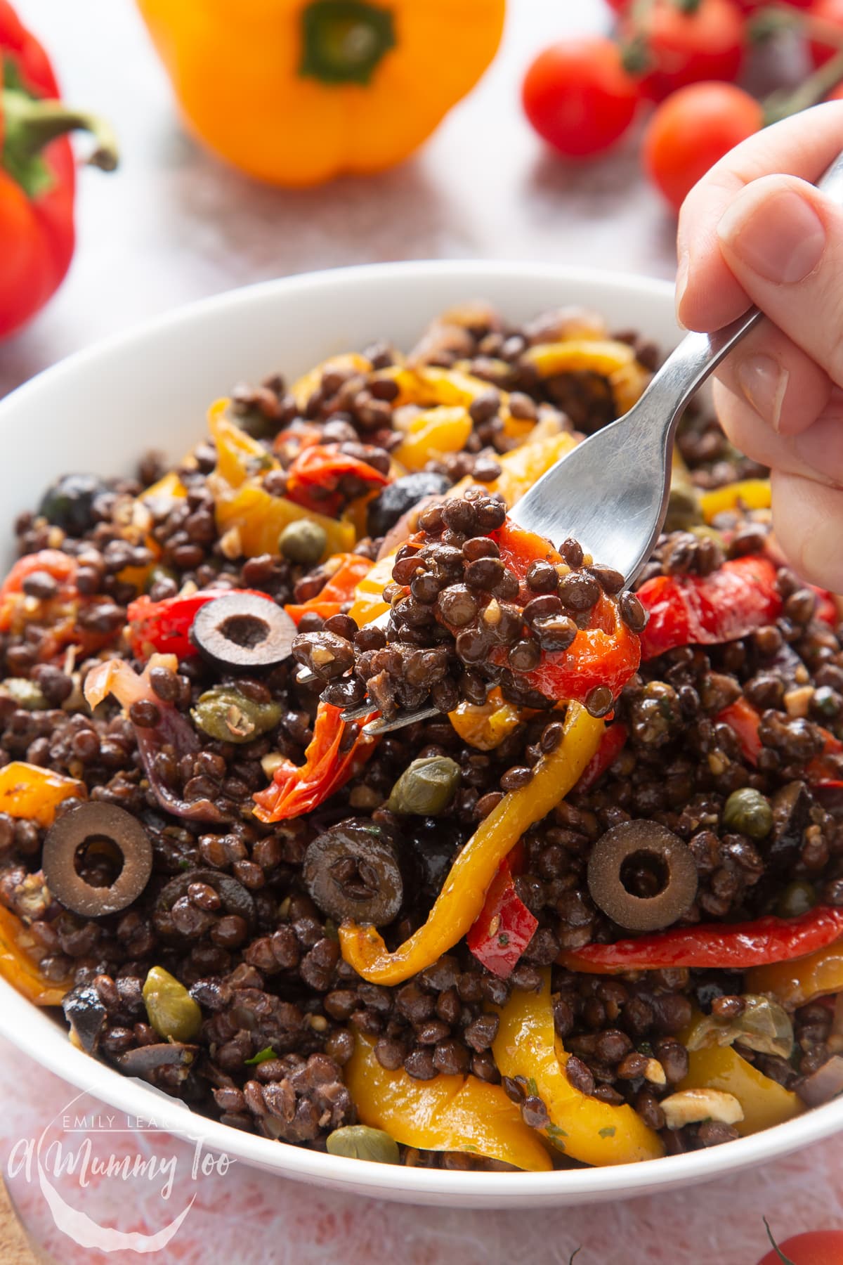 Vegan lentil salad served in a white shallow bowl. A hand delves a fork into the salad.