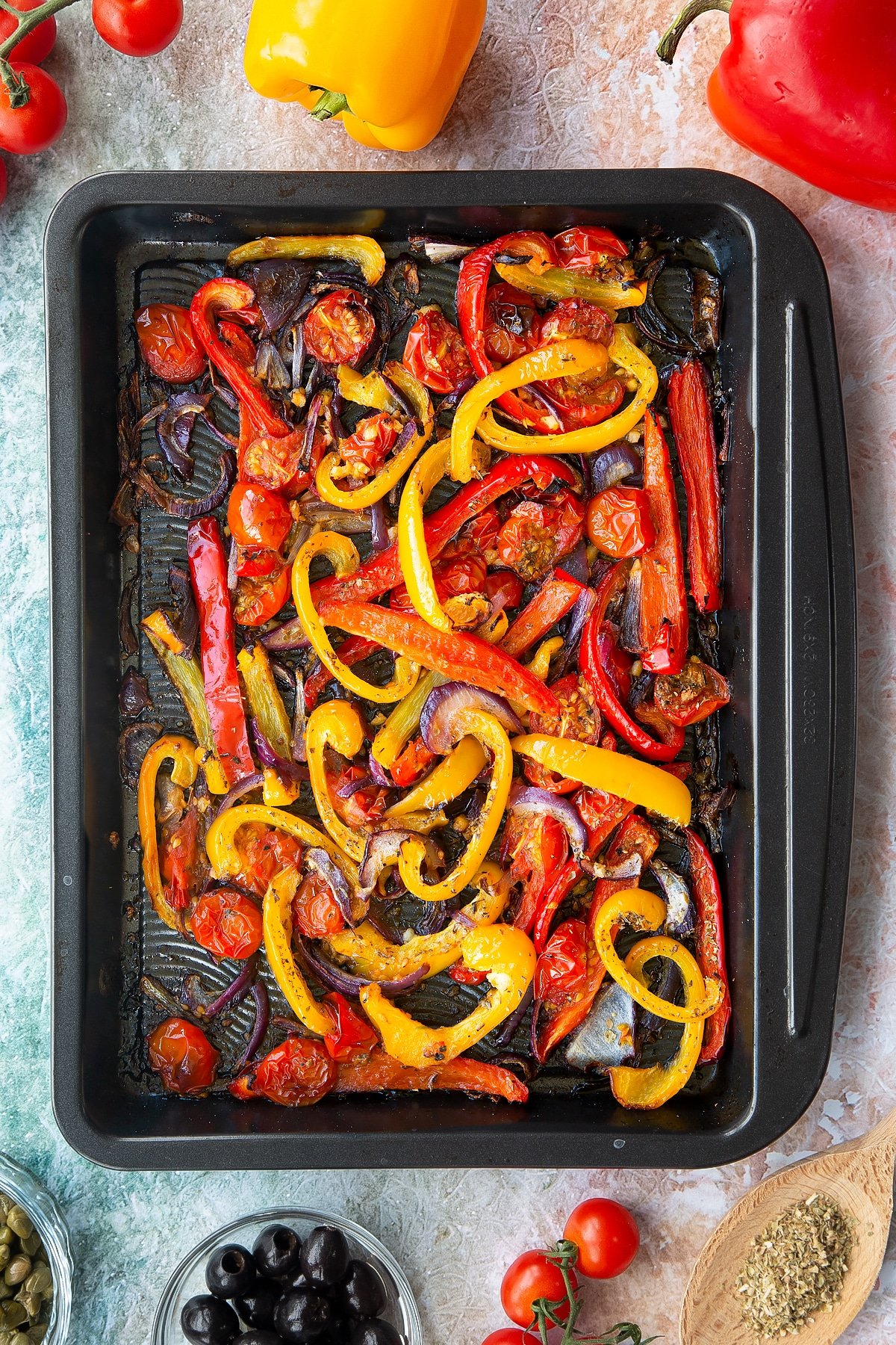 Roasted cherry tomatoes, peppers and onions in an oven tray. Ingredients to make vegan lentil salad surround the tray.