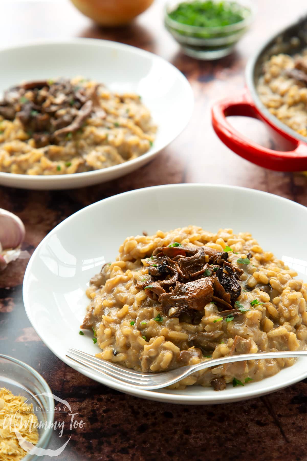 Vegan mushroom risotto in a shallow white bowl with a fork towards the front of the bowl. Shown from the side.