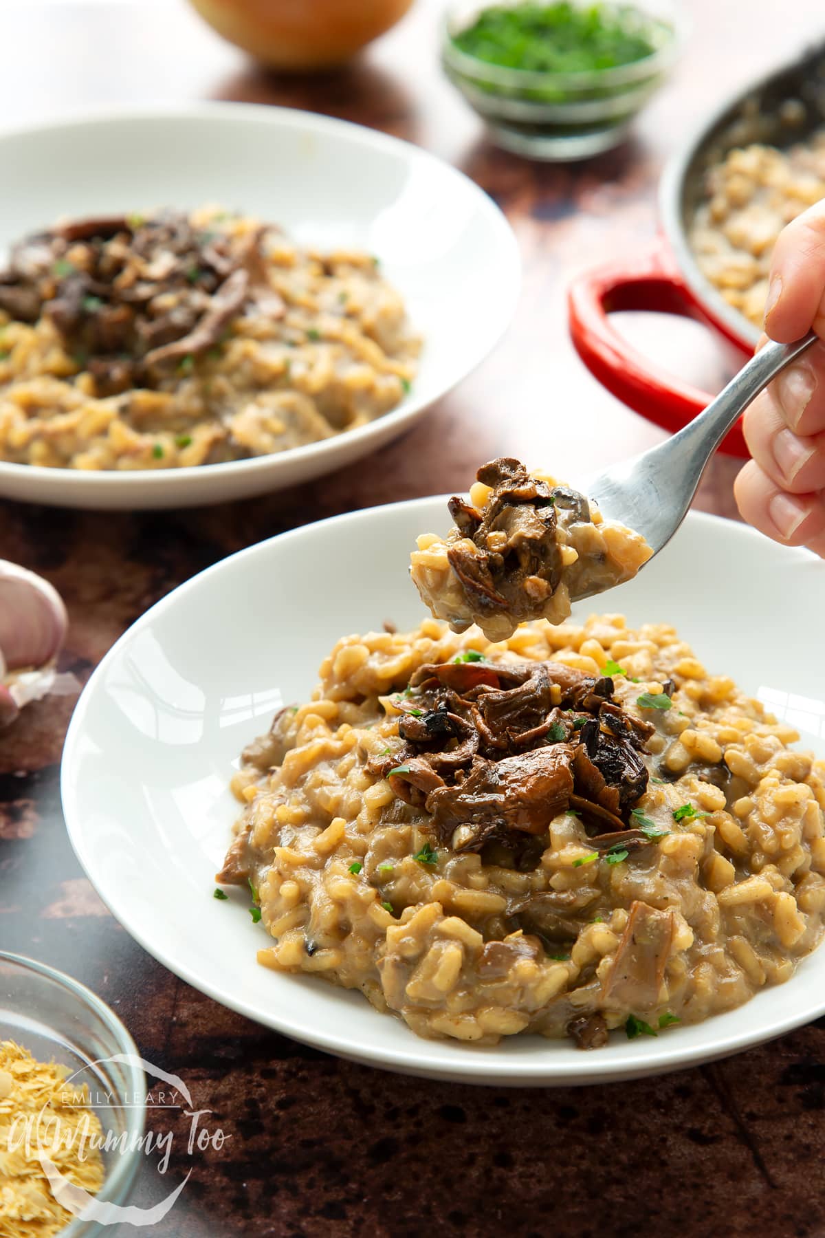 Vegan mushroom risotto in two shallow white bowls. A fork takes from of the risotto from the bowl in the foreground.