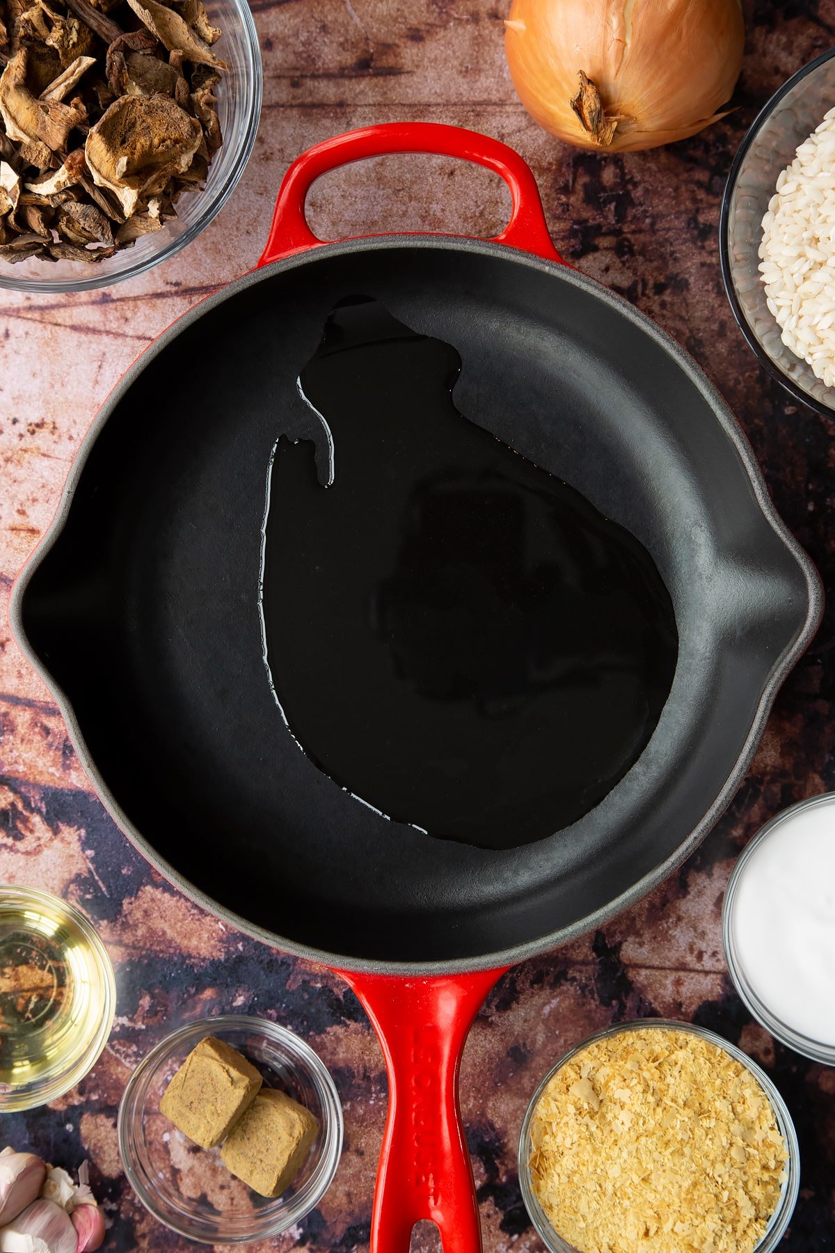 Oil in a pan. Ingredients to make vegan mushroom risotto surround the pan.