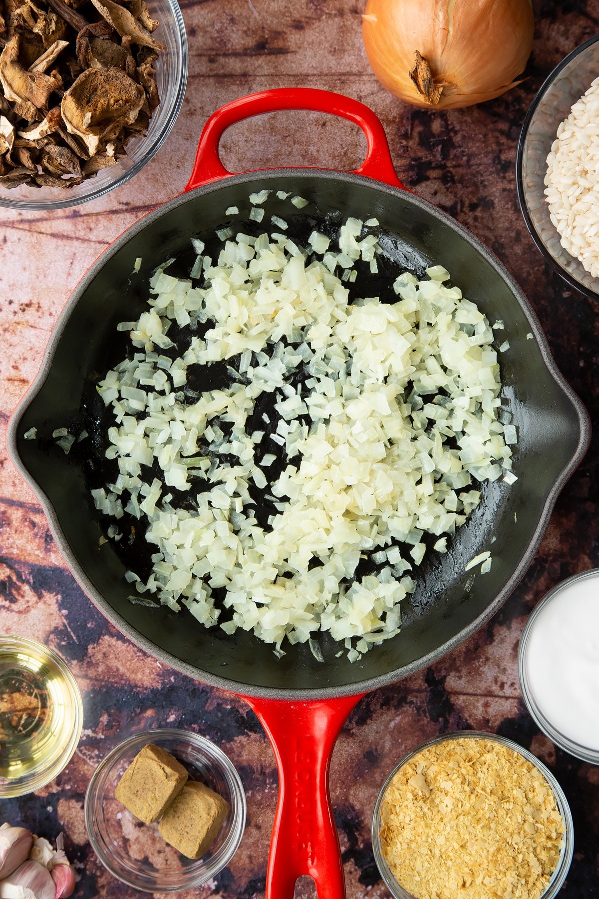 Lightly fried onions in a pan. Ingredients to make vegan mushroom risotto surround the pan.