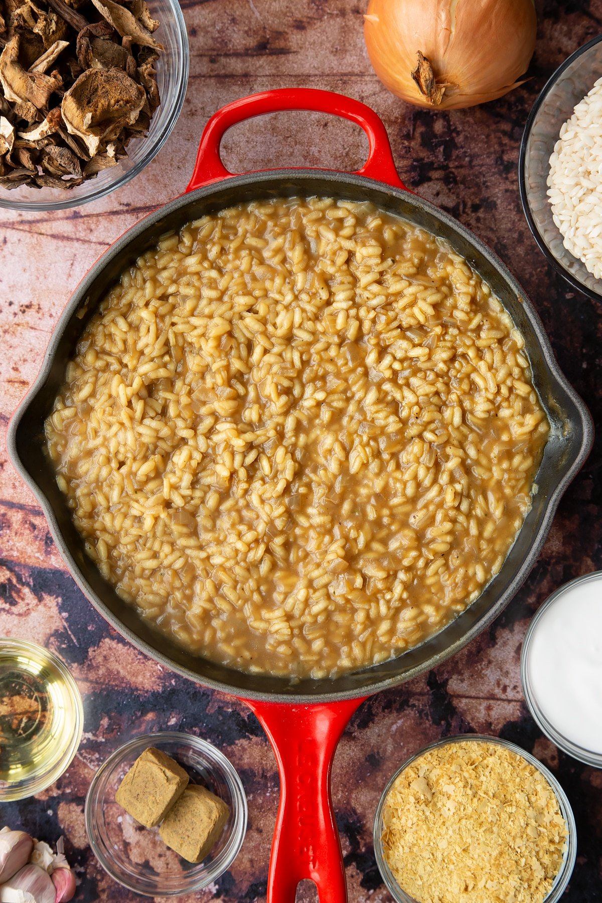 Mushroom risotto in a pan. Ingredients to make vegan mushroom risotto surround the pan.