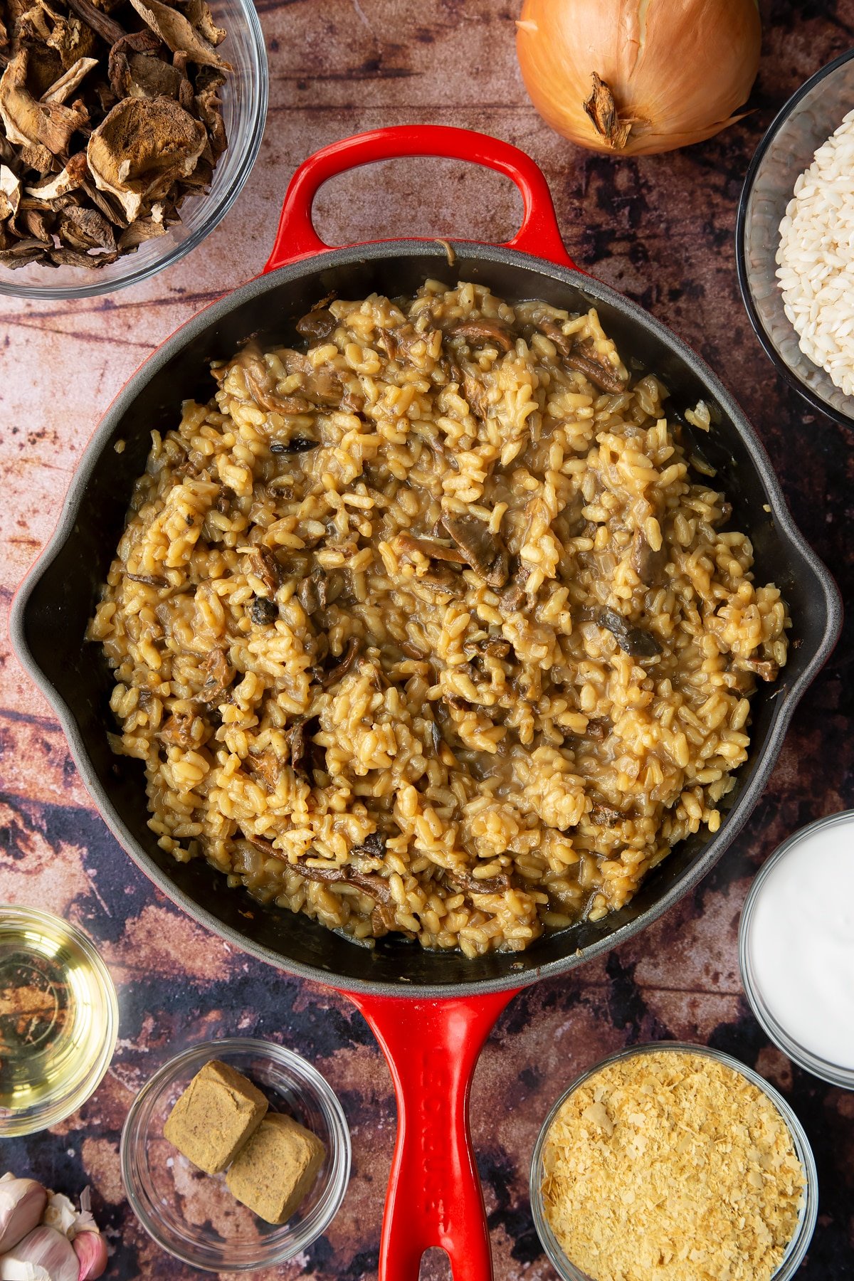 Mushroom risotto with fried porcini mushrooms in a pan. Ingredients to make vegan mushroom risotto surround the pan.