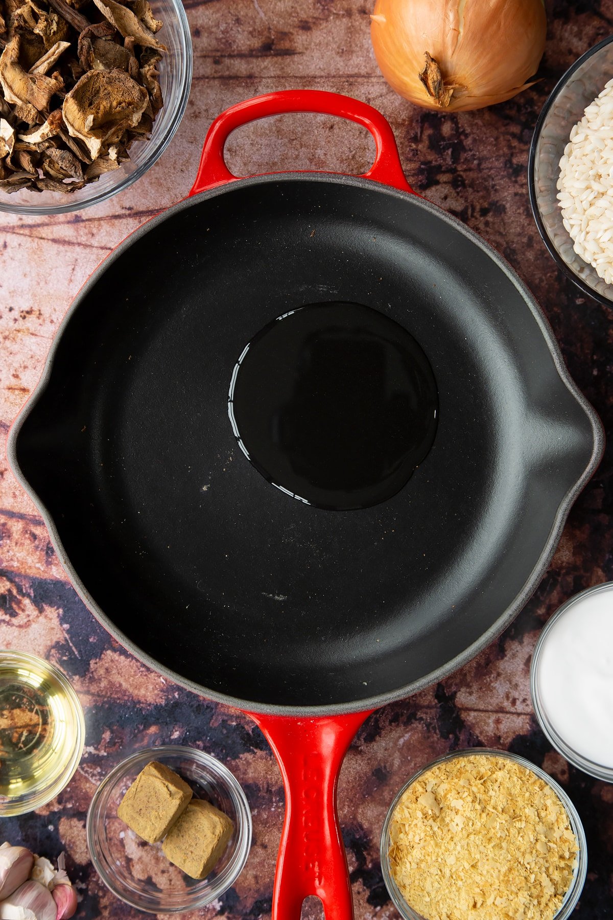 Oil in a pan. Ingredients to make vegan mushroom risotto surround the pan.