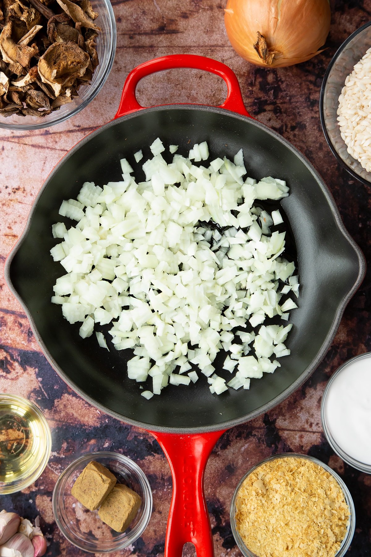 Oil and chopped onions in a pan. Ingredients to make vegan mushroom risotto surround the pan.