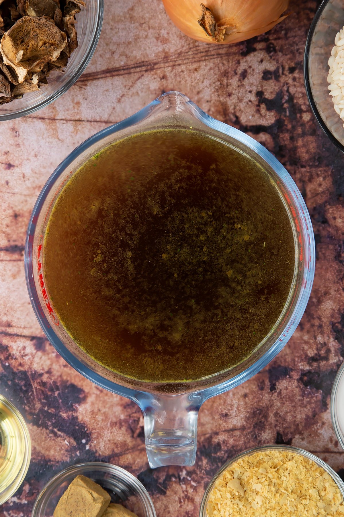 Mushroom stock in a glass jug. Ingredients to make vegan mushroom risotto surround the jug.