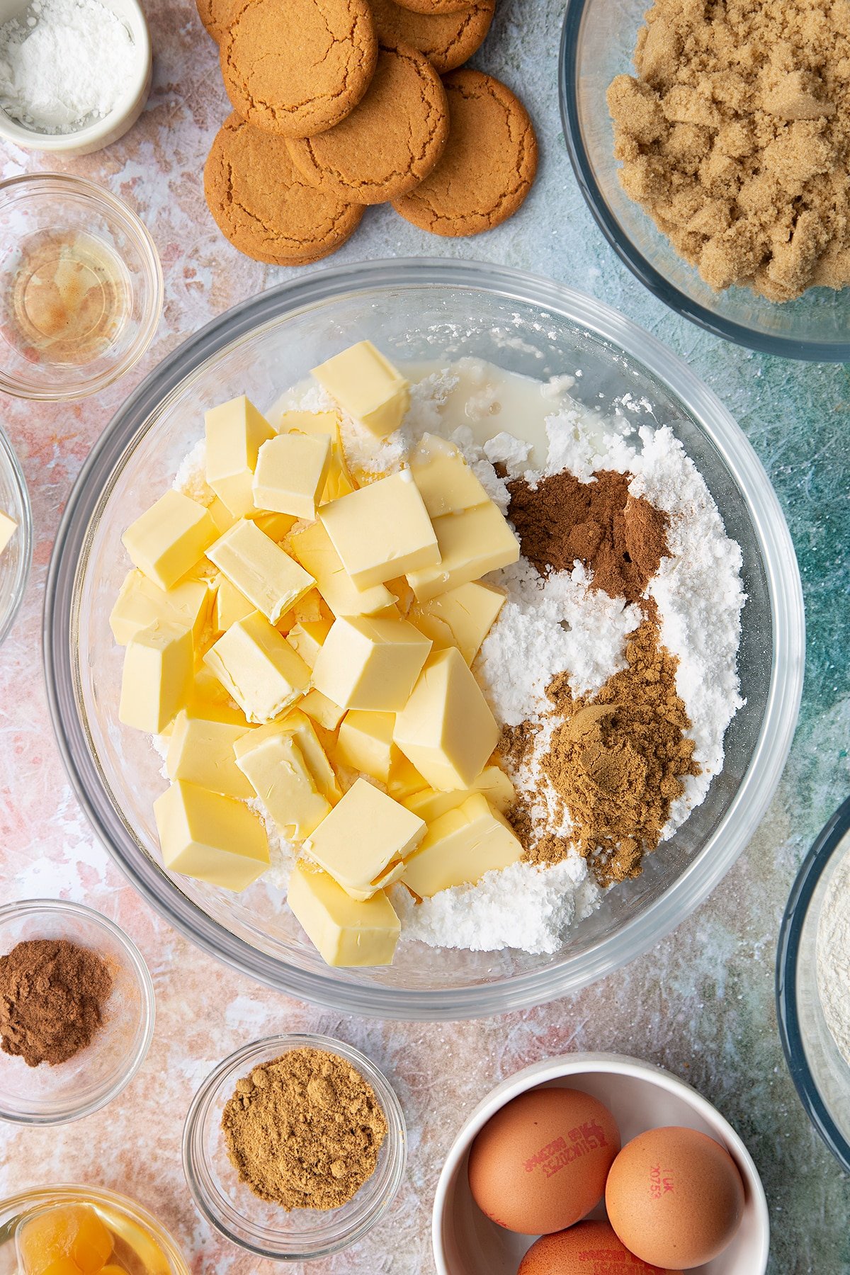 Icing sugar, butter, cinnamon, ginger, vanilla and milk in a large bowl. Ingredients to make ginger cupcakes surround the bowl.