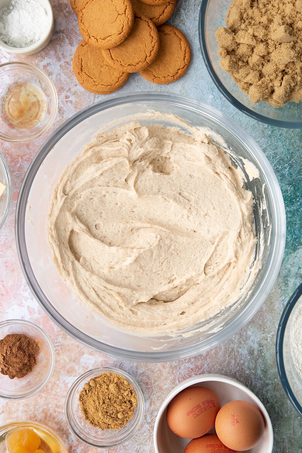 Ginger buttercream in a large bowl. Ingredients to make ginger cupcakes surround the bowl.