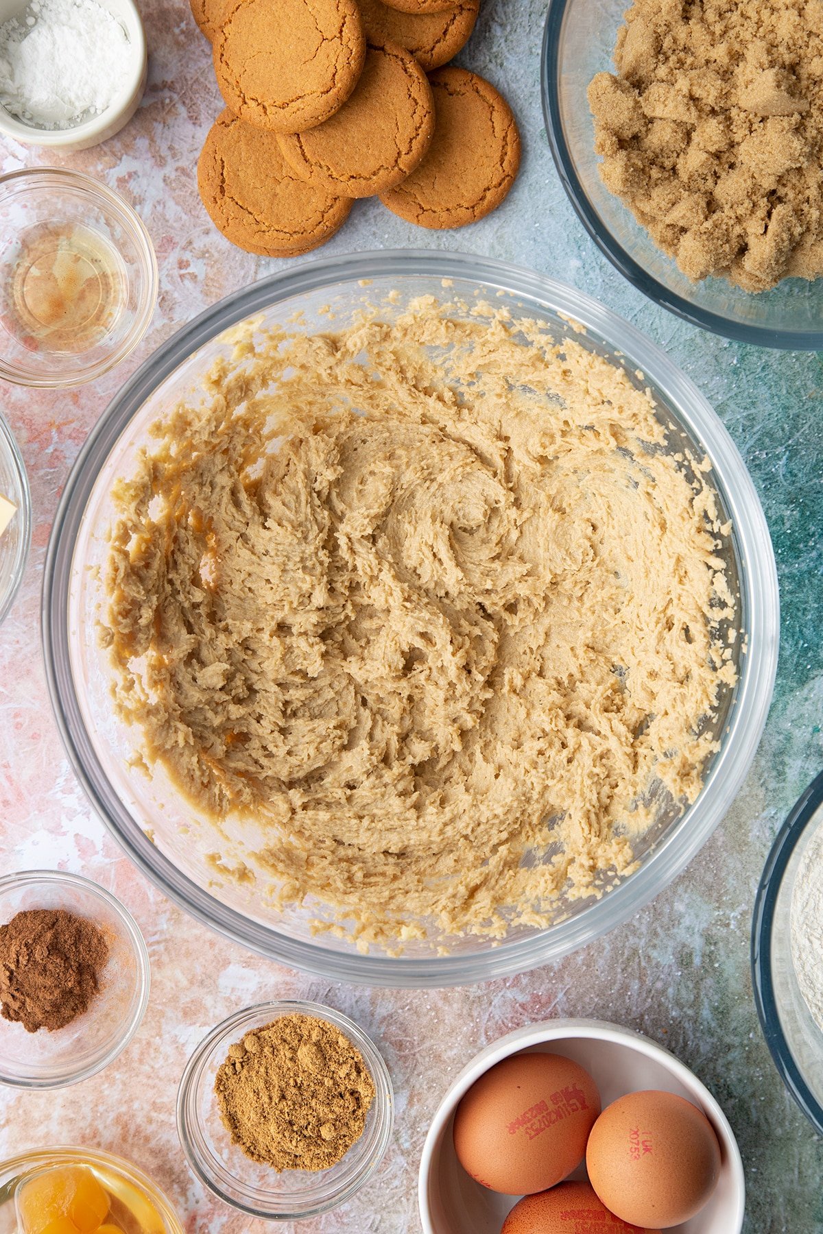 Butter and soft light brown sugar whisked together in a mixing bowl. Ingredients to make ginger cupcakes surround the bowl.