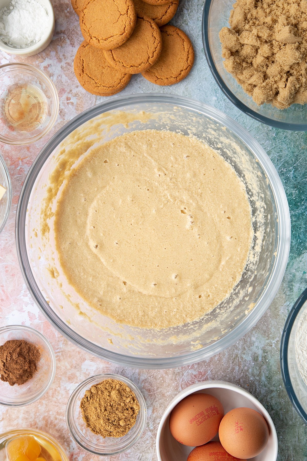 Butter, soft light brown sugar, milk, eggs and vanilla whisked together in a mixing bowl. Ingredients to make ginger cupcakes surround the bowl.