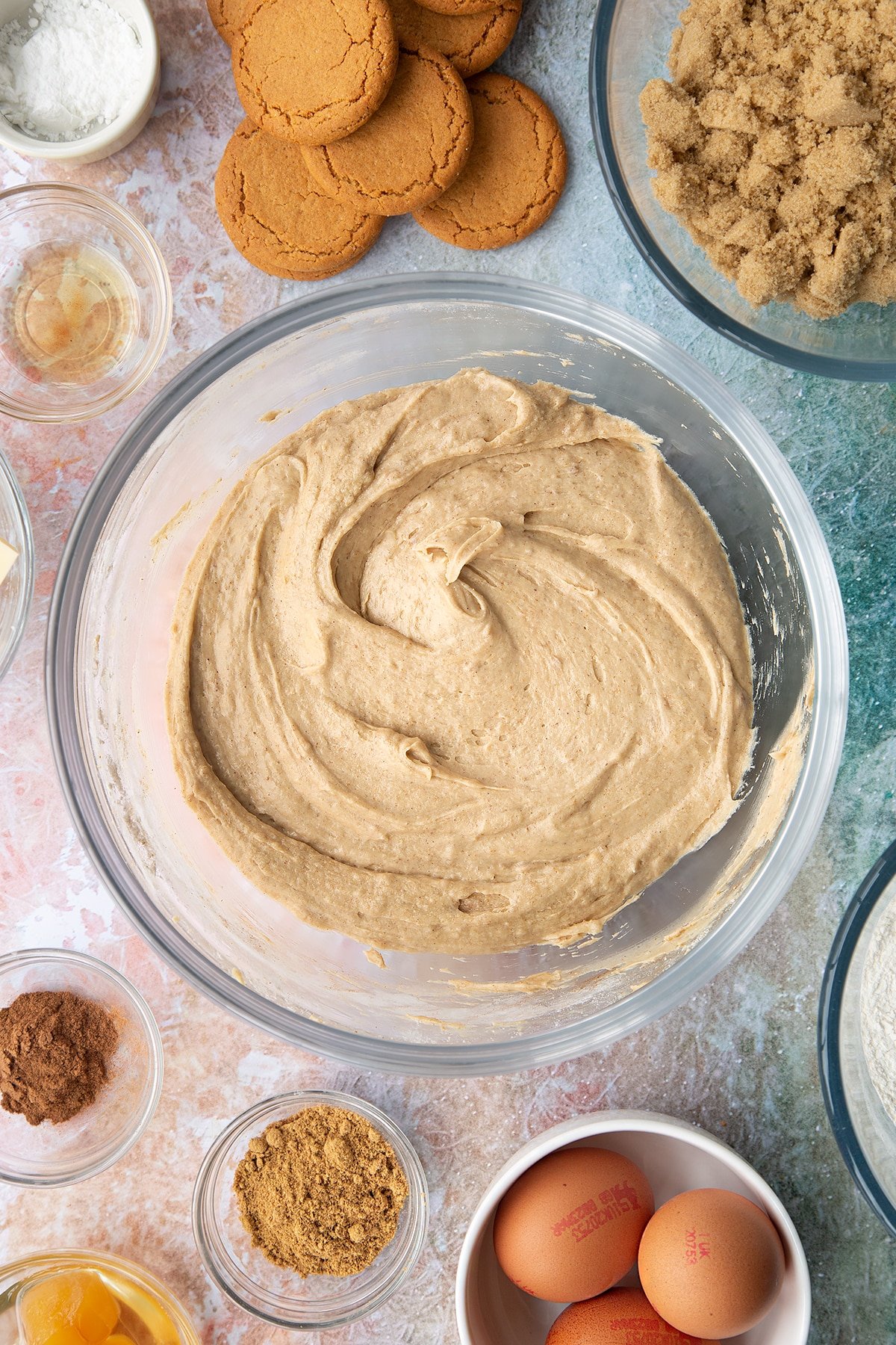 Ginger cake batter in a mixing bowl. Ingredients to make ginger cupcakes surround the bowl.