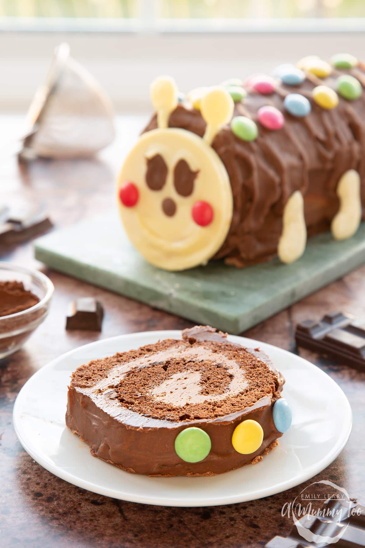 A slice of caterpillar cake on a small white plate with the caterpillar cake in the background.