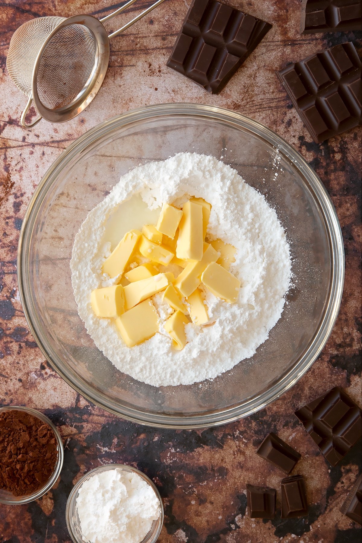 Butter, milk, vanilla and icing sugar in a glass mixing bowl. Ingredients for the caterpillar cake recipe surround the bowl.