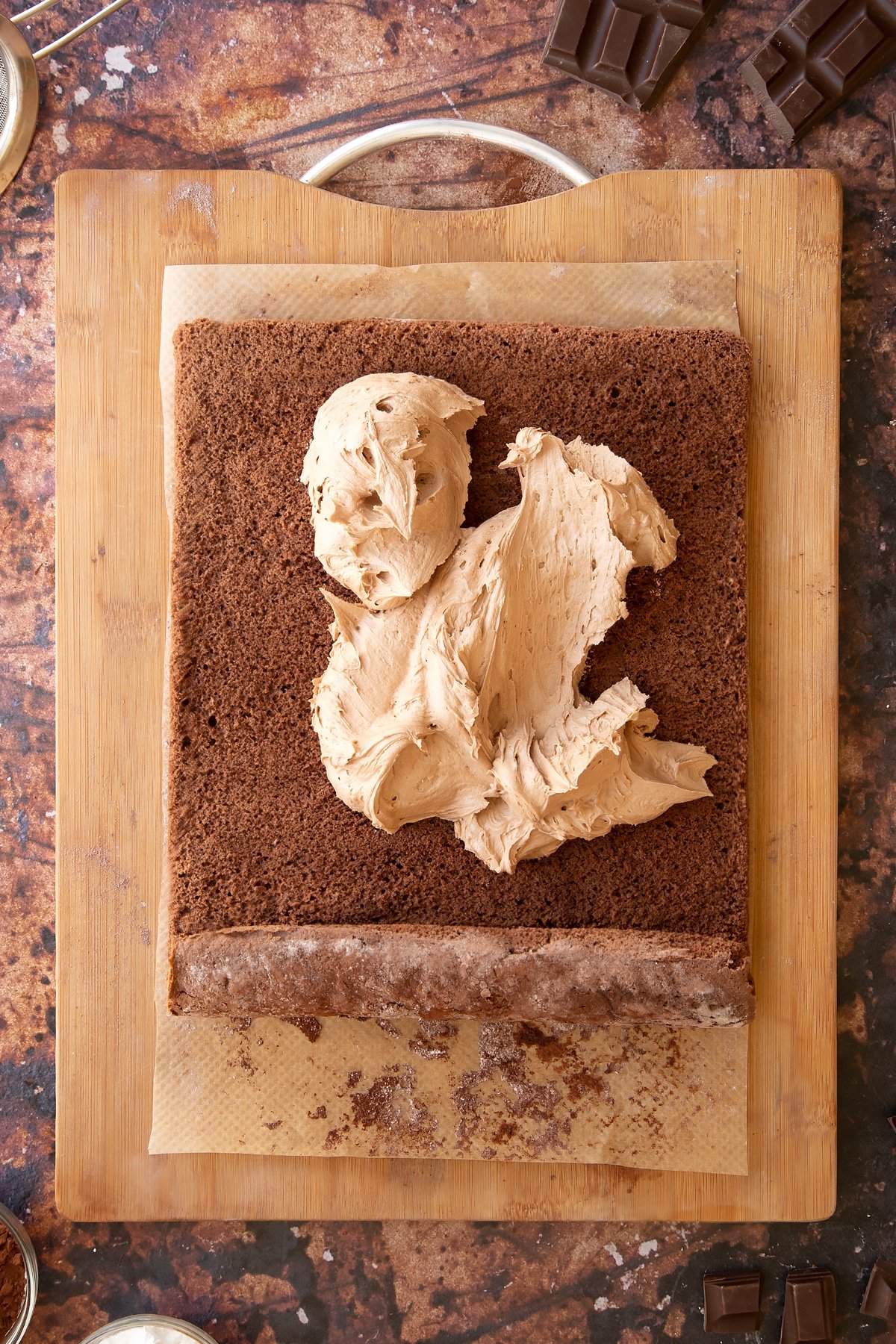 A chocolate sponge unrolled on a wooden board. The sponge is topped with dollops of chocolate buttercream.