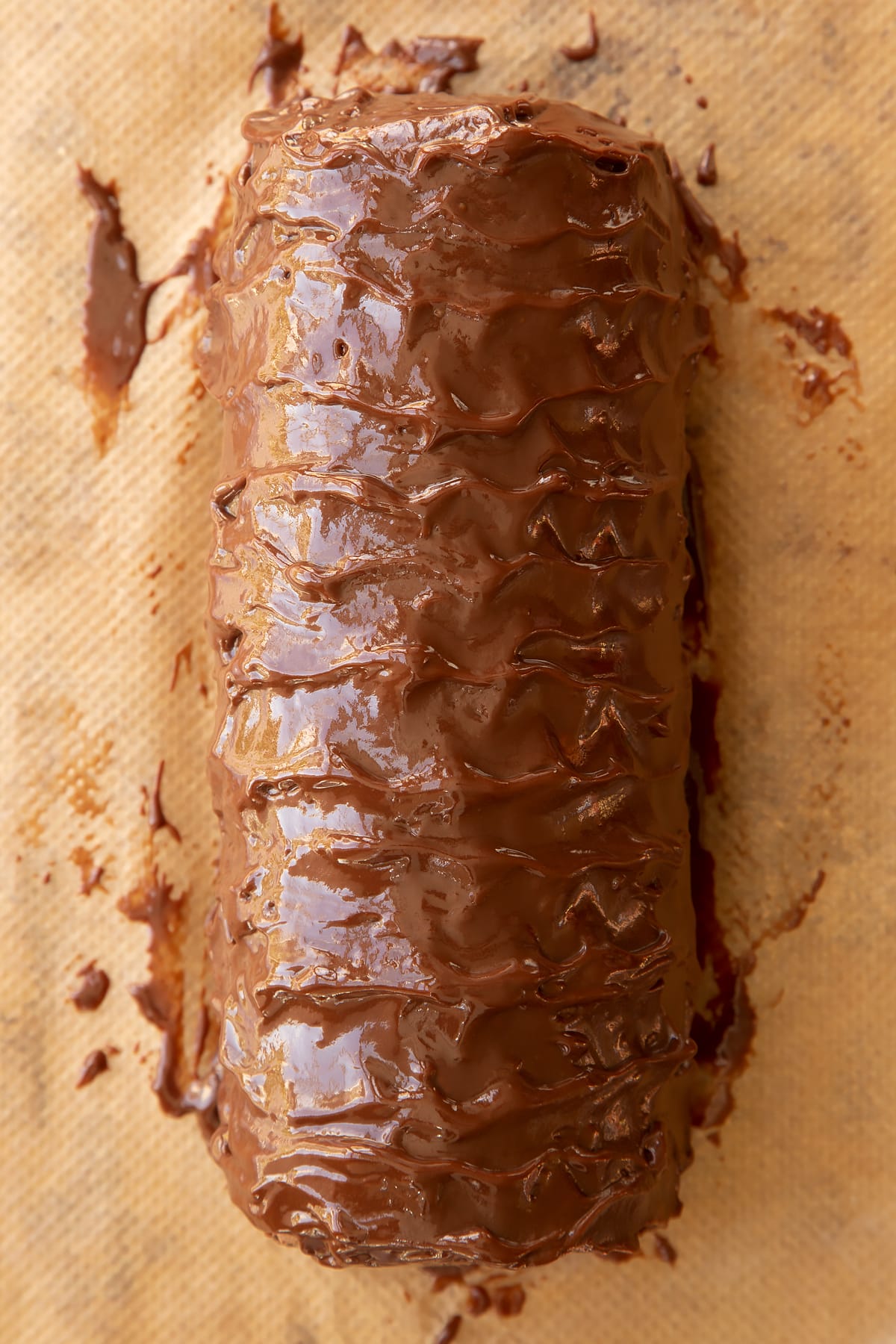 Chocolate Swiss roll covered with chocolate ganache on baking paper.