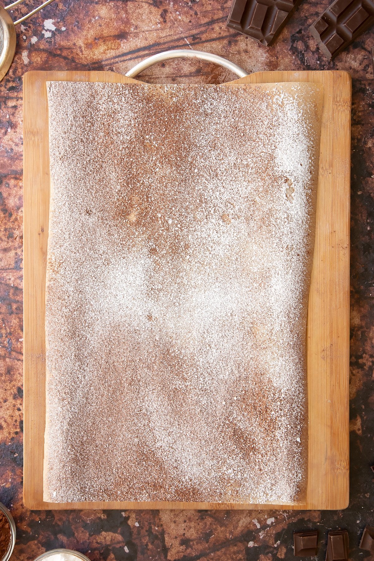 A wooden board and baking paper dusted with cocoa and icing sugar. 