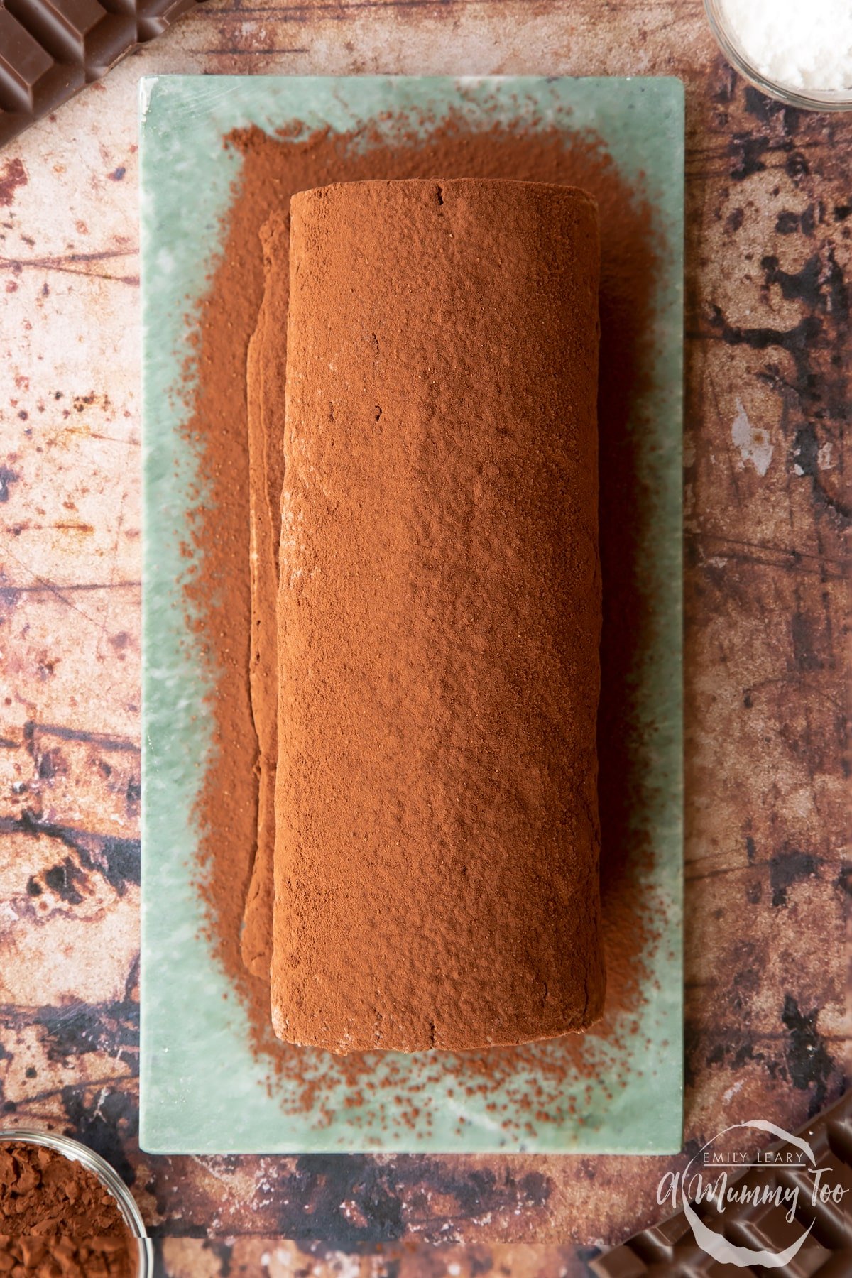 Chocolate Swiss roll dusted with cocoa on a grey marble board, shown from above. 