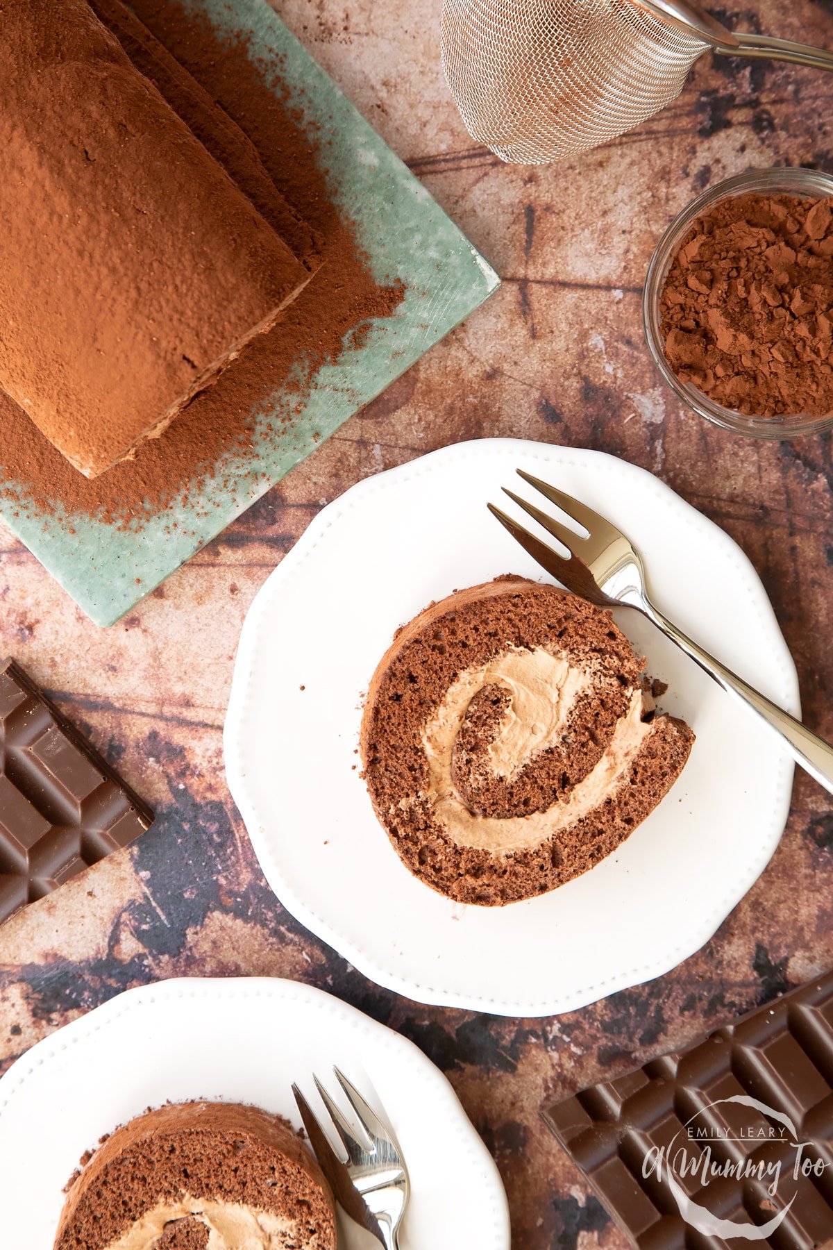 Two slices of Chocolate Swiss roll on white plates with forks, shown from above.