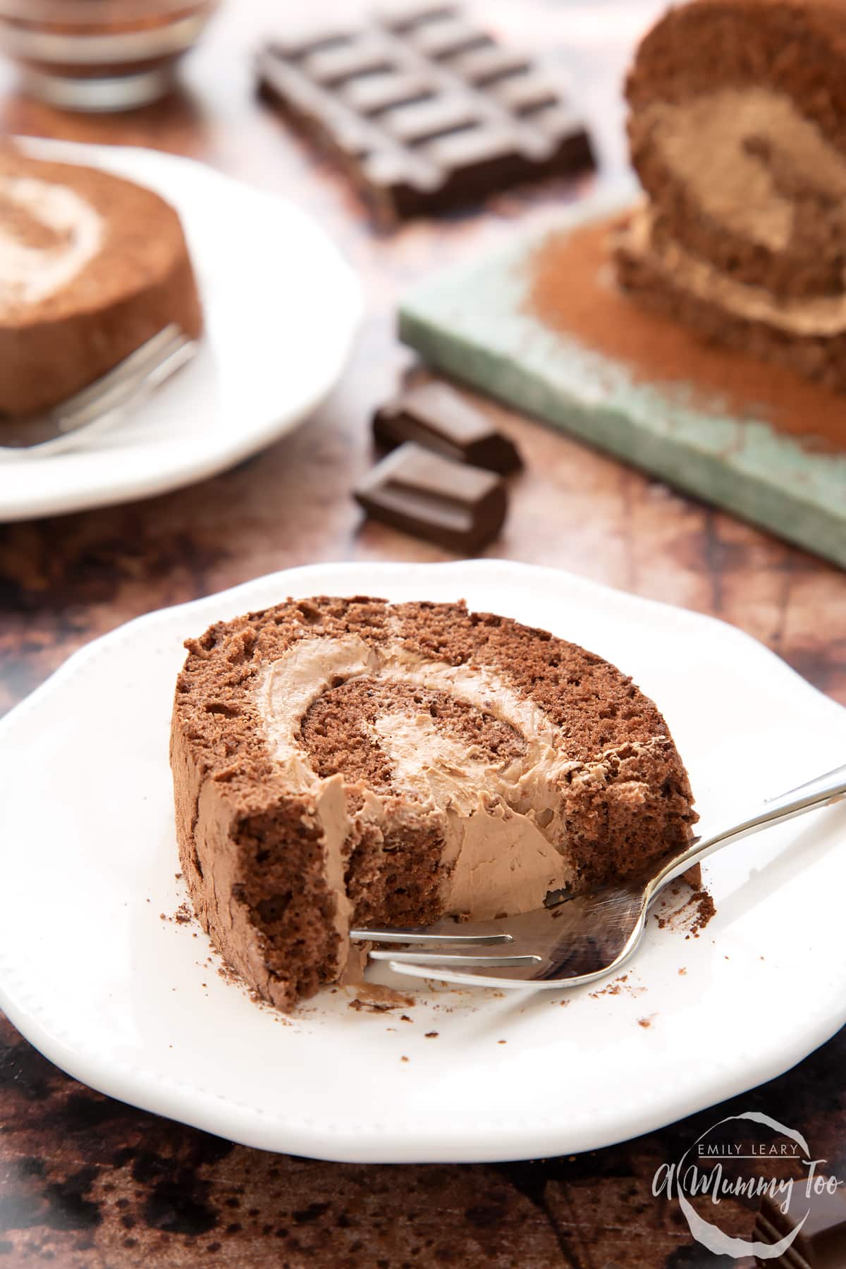 A slice of Chocolate Swiss roll on a white plate with a fork. Some of it has been eaten.