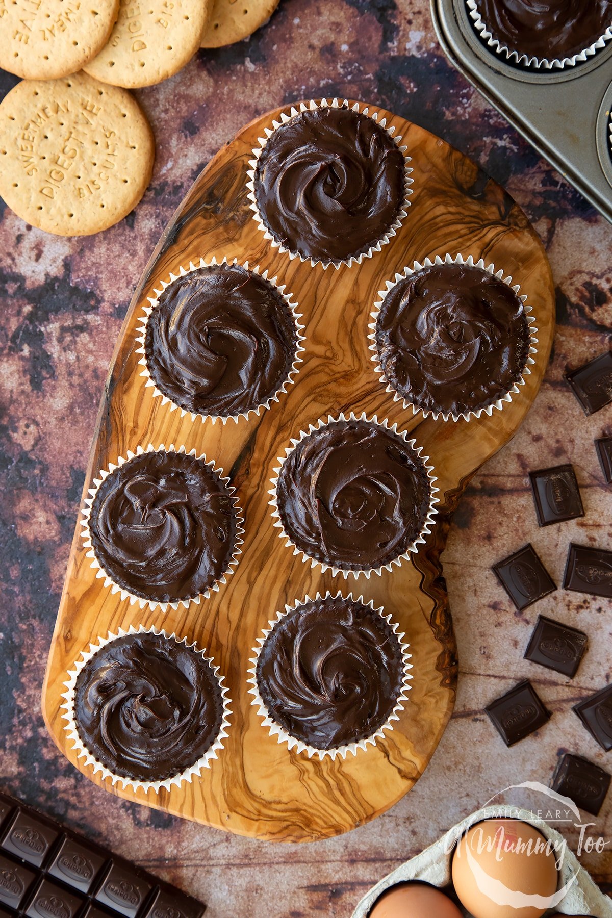 Chocolate cheesecake cupcakes in rows on an olive wood board, shown from above. 