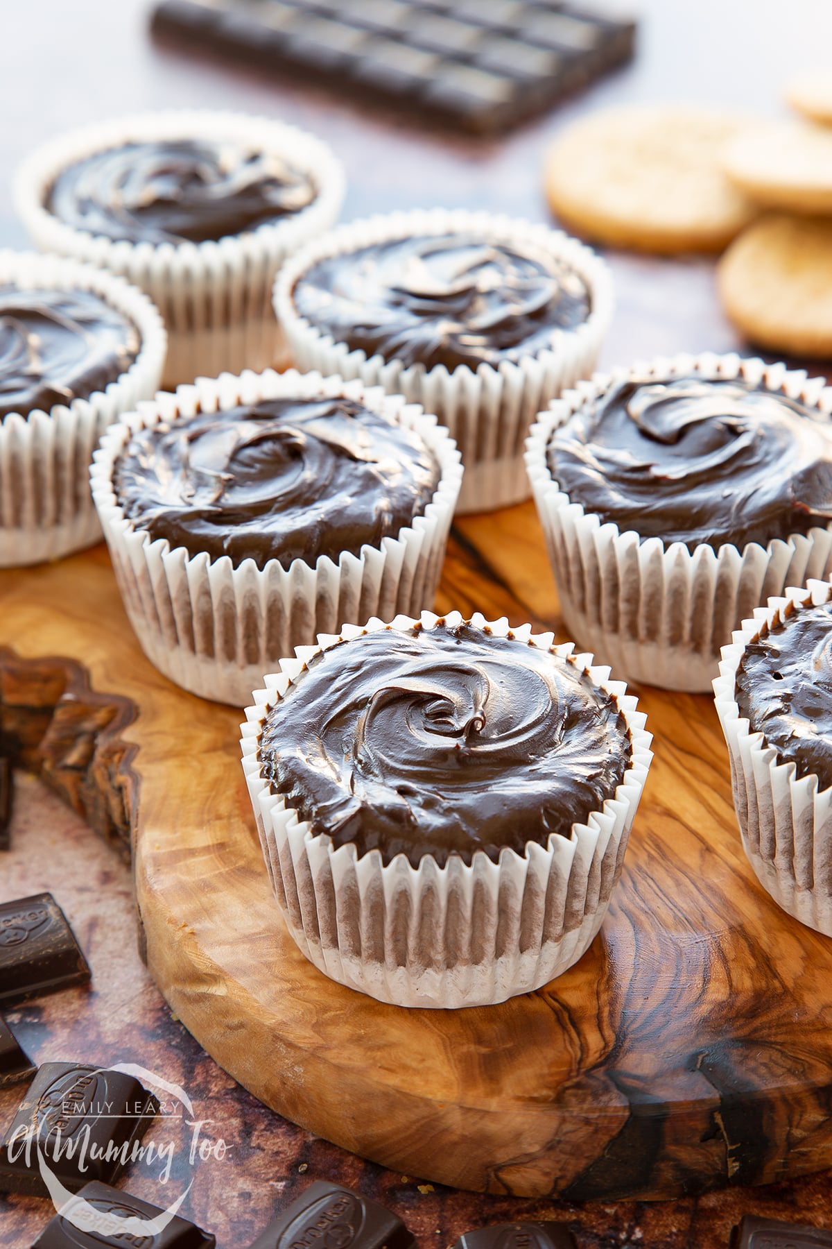 Chocolate cheesecake cupcakes topped with dark chocolate ganache in rows on an olive wood board. 
