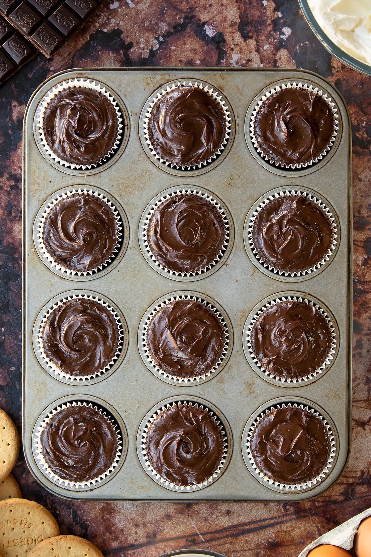 Chocolate cheesecake cupcakes freshly topped with ganache in a muffin tray. 